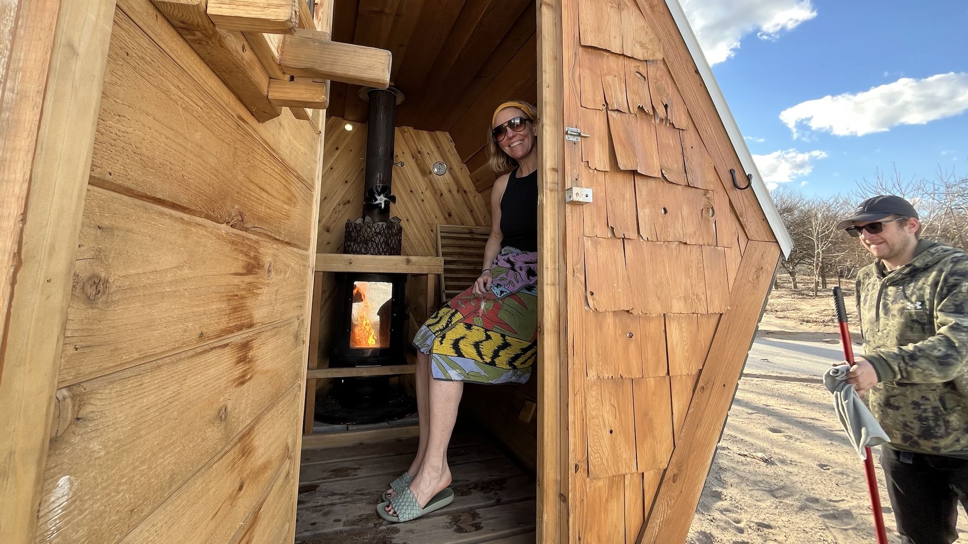 A woman sitting inside a cedar sauna wearing a black top and a towel around her waist.
