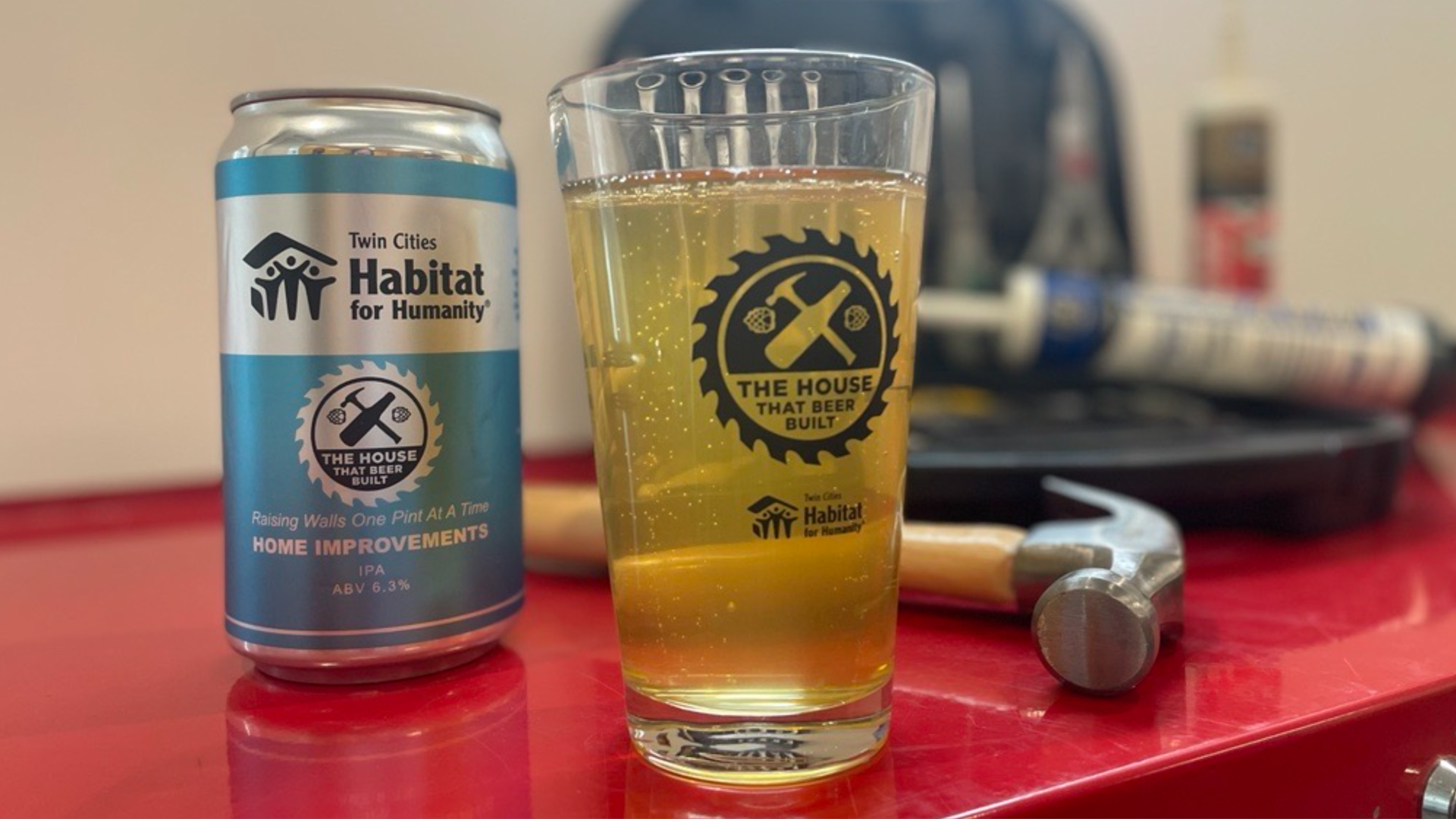 A can of beer and beer in a pint glass, next to a hammer.