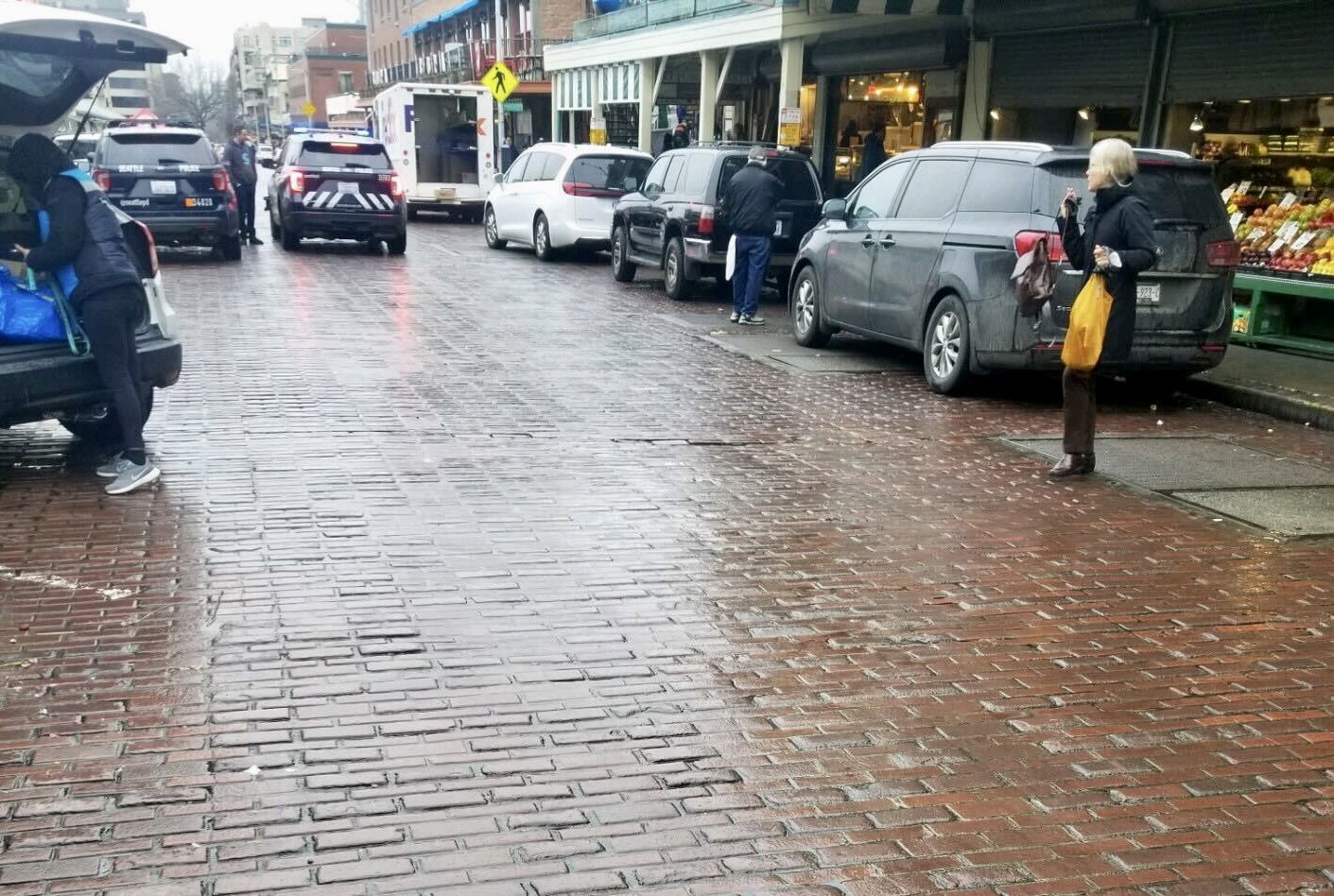 A view of wet cobblestones and cars along the street. 