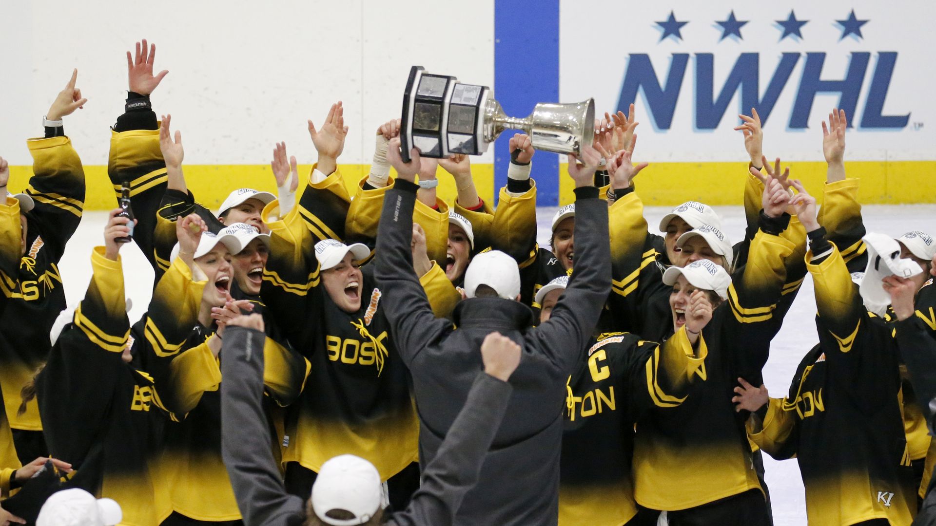 Boston Pride players cheer as coach Paul Mara hoists the NWHL Isobel Cup trophy after the team's win over the Minnesota Whitecaps in the championship hockey game in Boston, Saturday, March 27, 2021