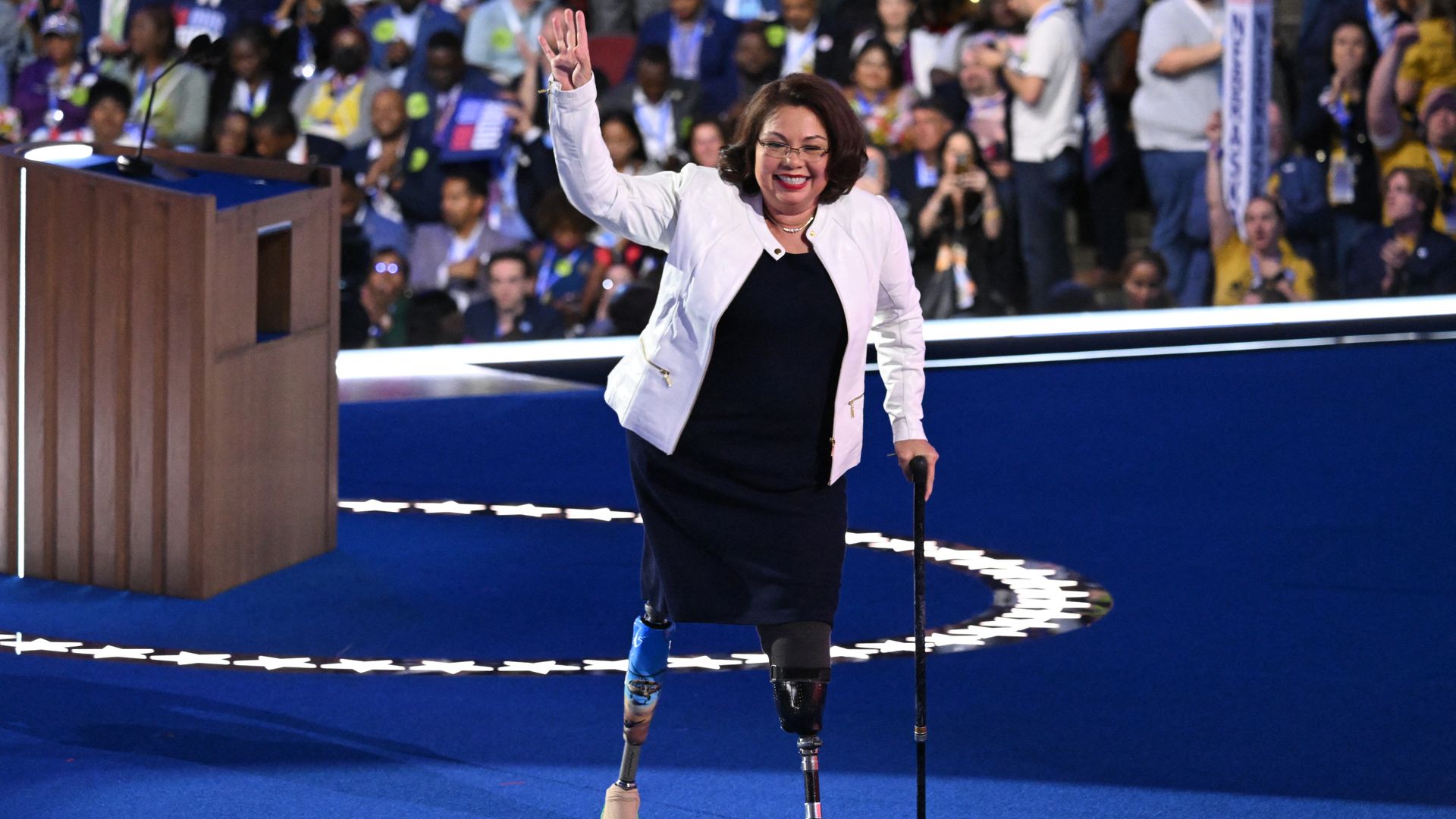 Photo of a woman with prosthetic legs using a cane to walk away from a podium 