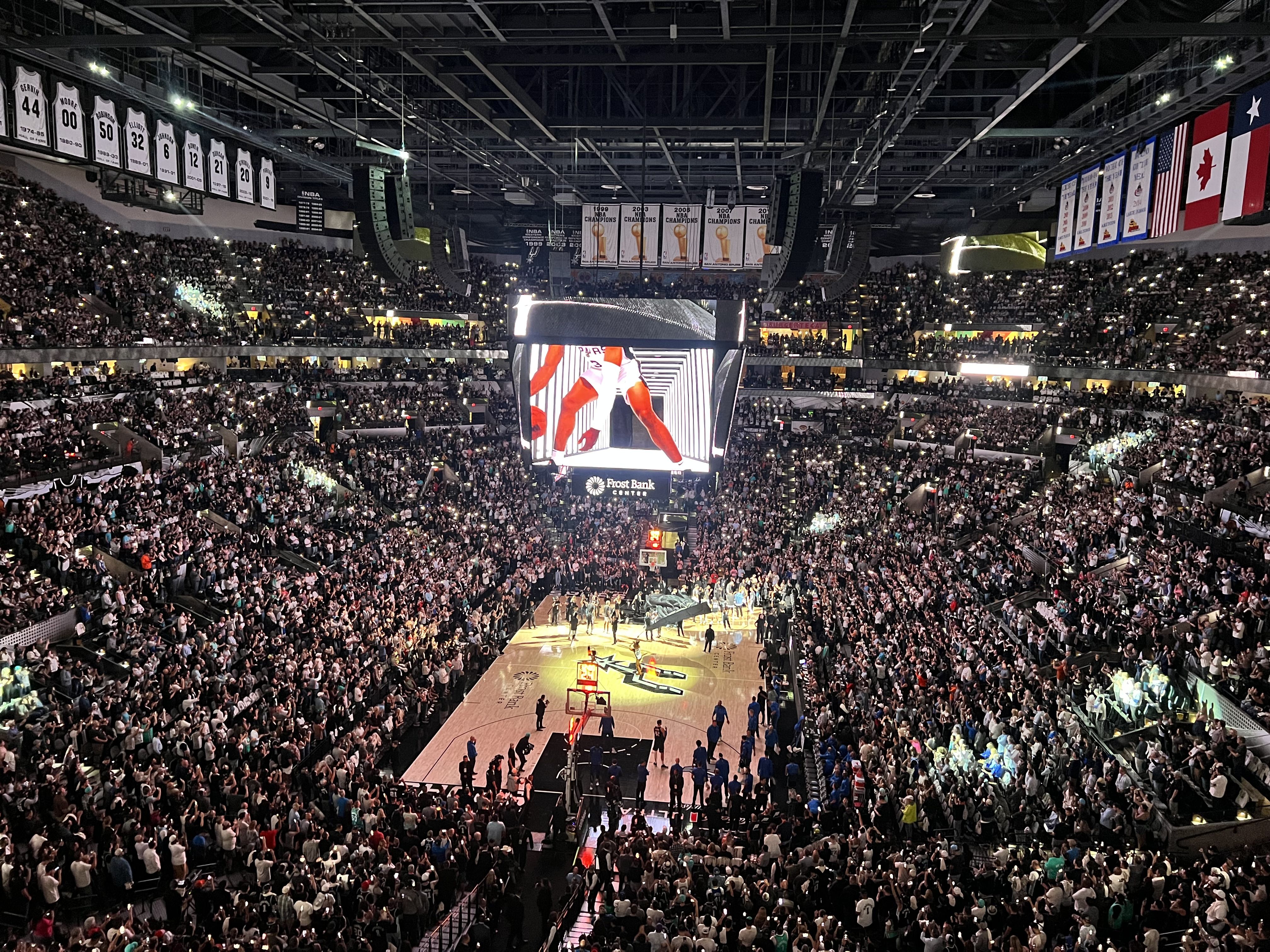 A mostly full basketball arena illuminated by cellphone lights held by fans. 