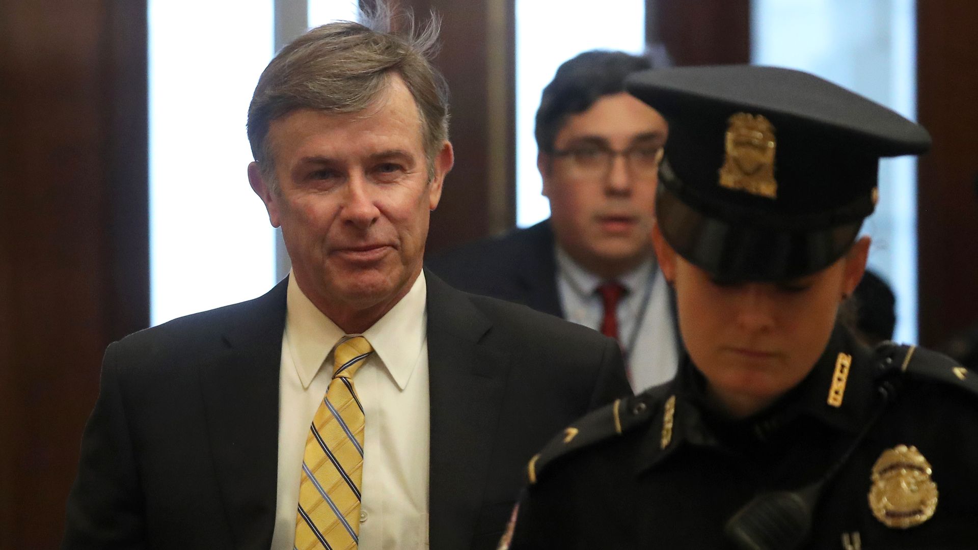 In this image, Joseph Maguire walks down a hallway while wearing a tie.