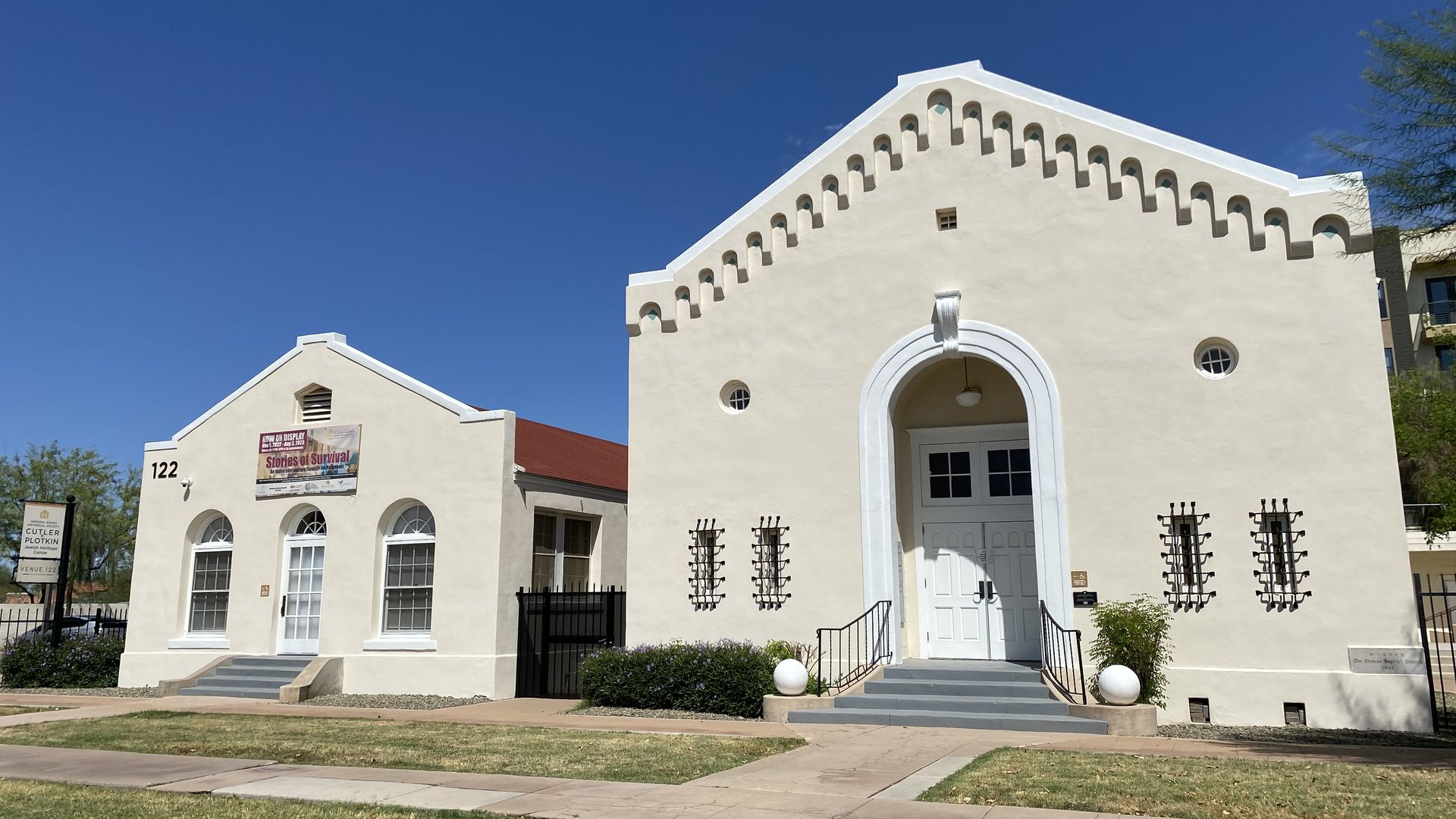An off white building with a triangular roof and an arched doorway next to a smaller similar building.