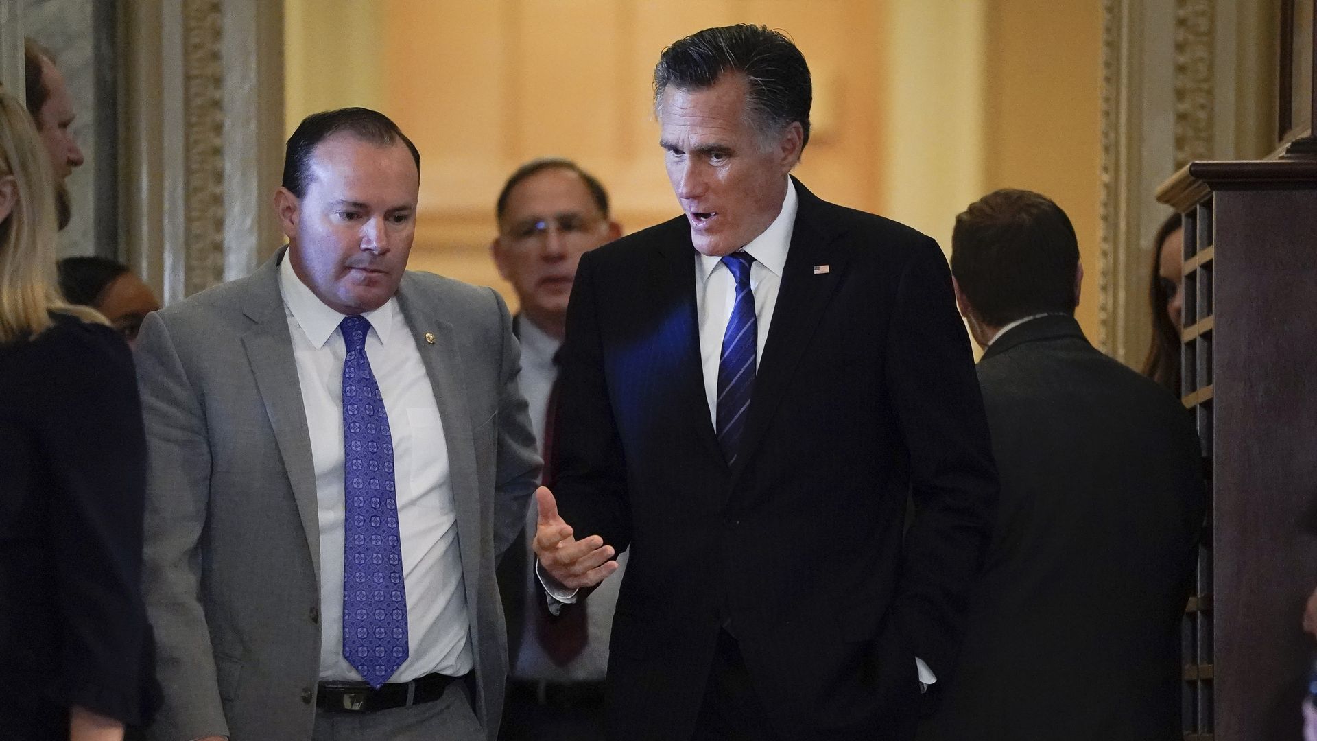 Utah Sens. Mike Lee and Mitt Romney walk down a hallway while talking.