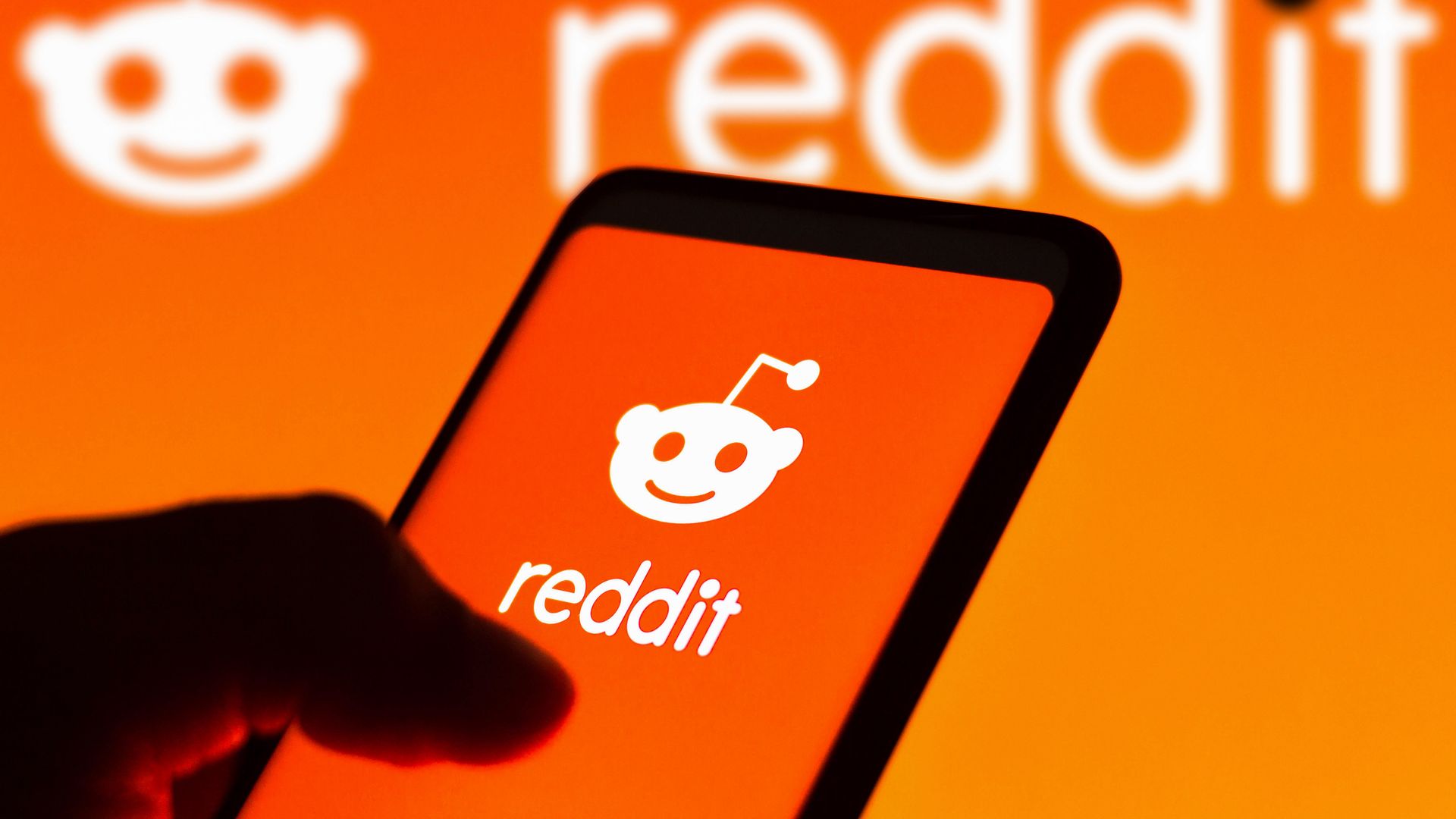 A person holding a smartphone with a Reddit logo on it.