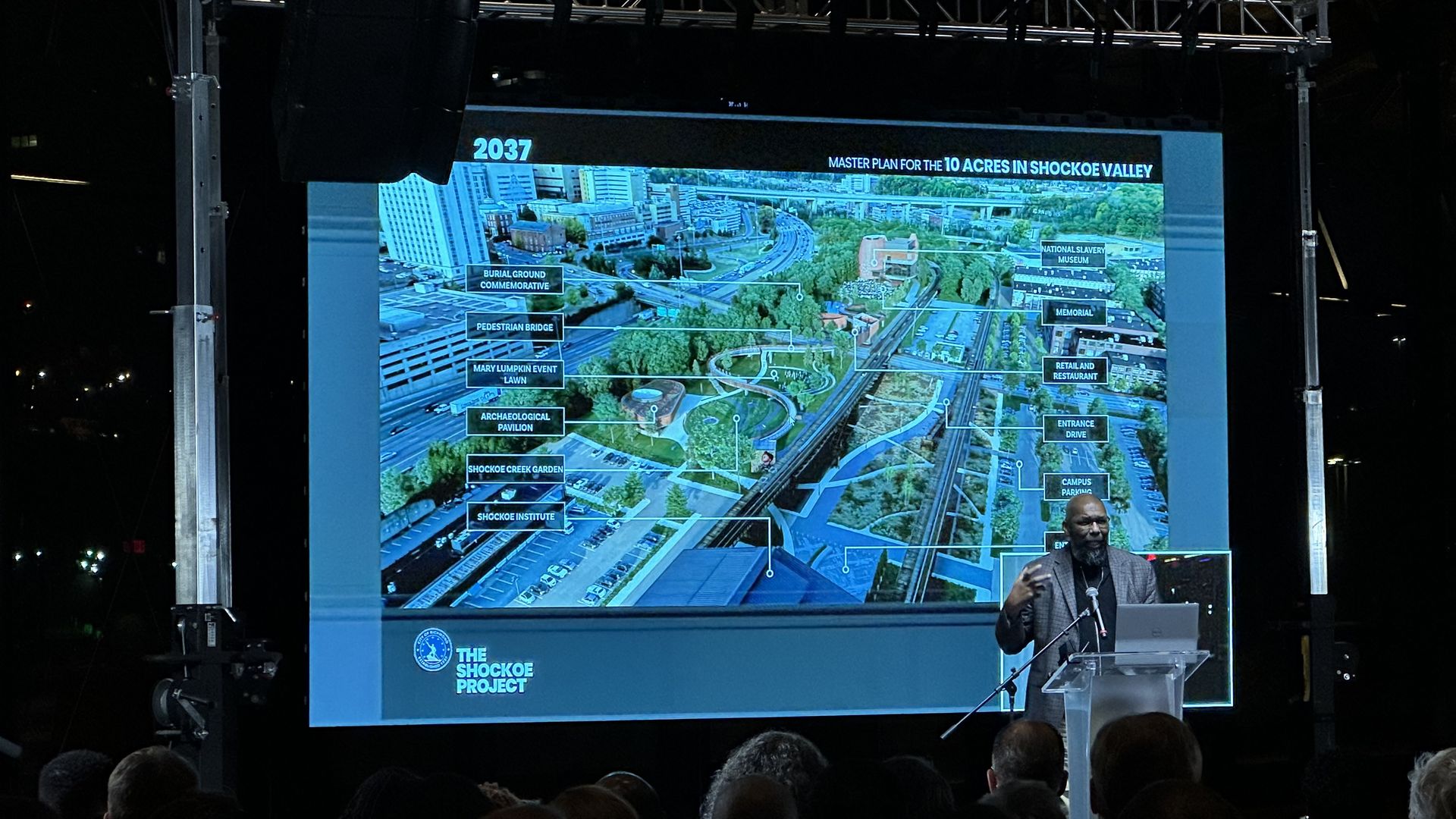 A man stands infront of a screen with a plan on it