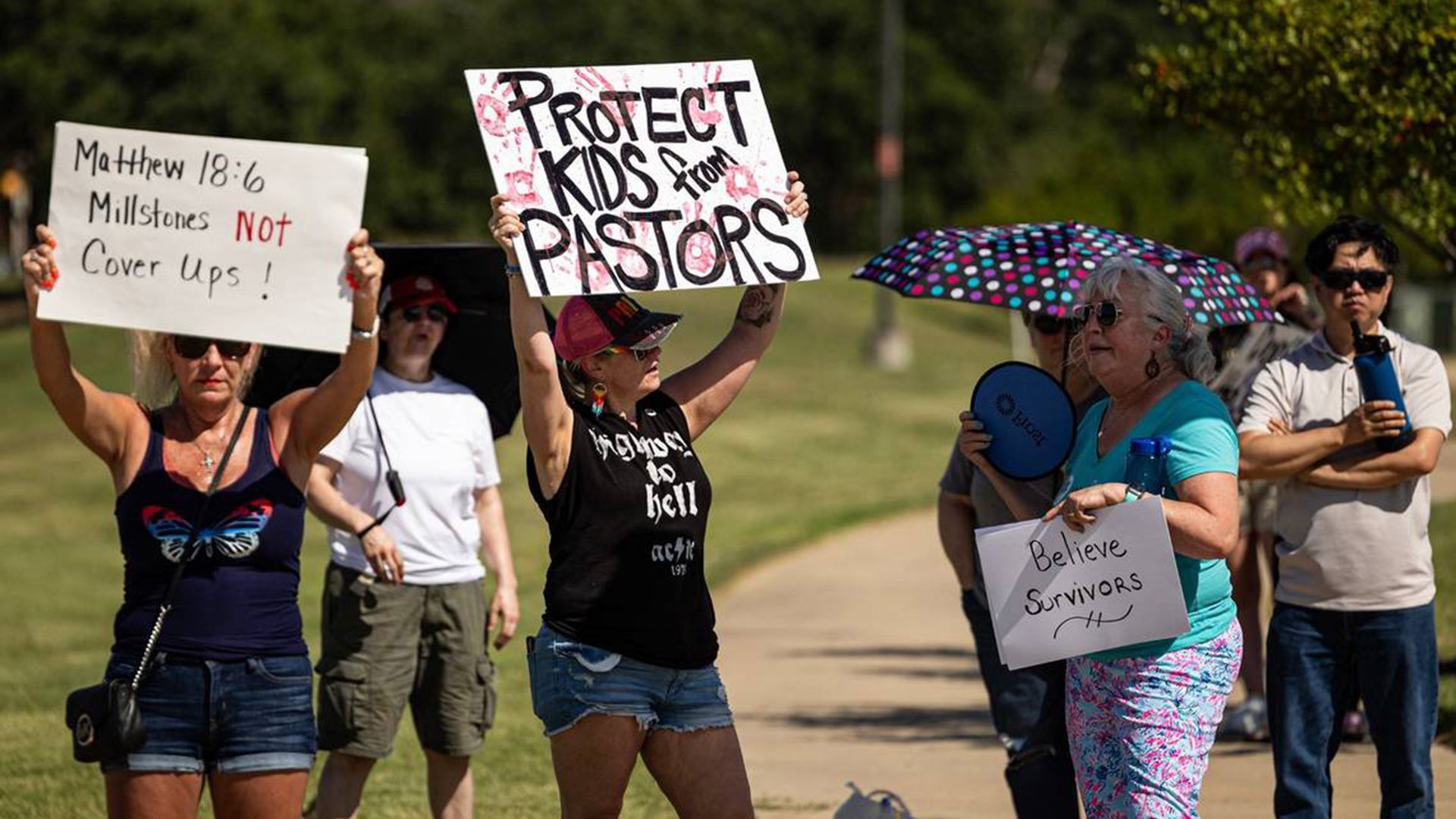 Protesters holding up signs that say "protect kids from pastors" and "believe survivors"