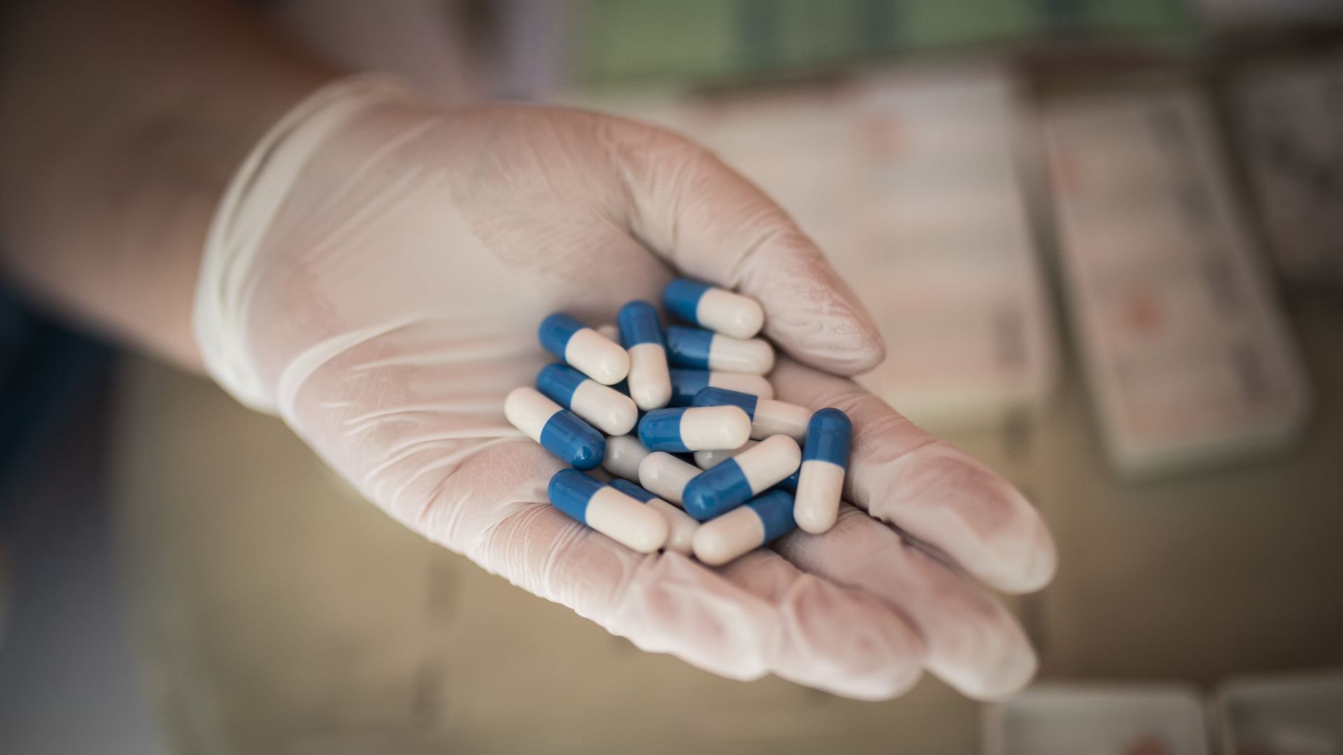 A gloved hand holds a dozen pills.