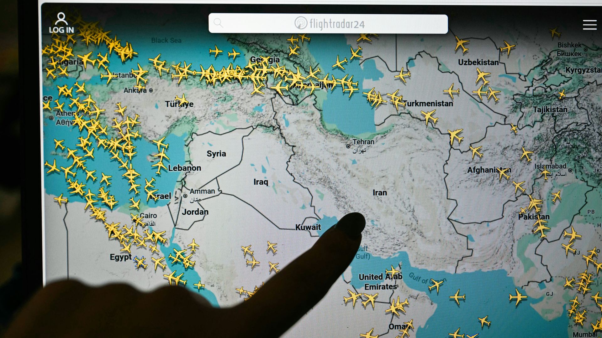 A hand points at a computer screen displaying a Flightradar24 map with commercial flights rerouted around Iran and Iraq.