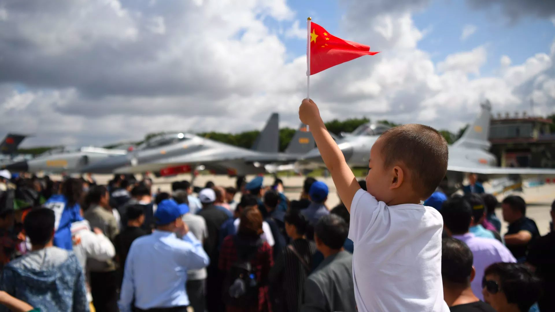 Photo of boy on someone's shoulders holding a China flag at a military parade