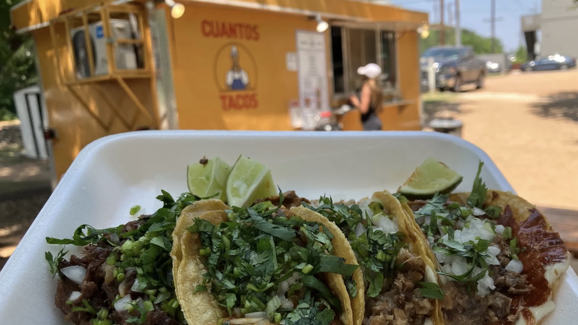 A photo of three tacos on a tray with a food truck in the background.
