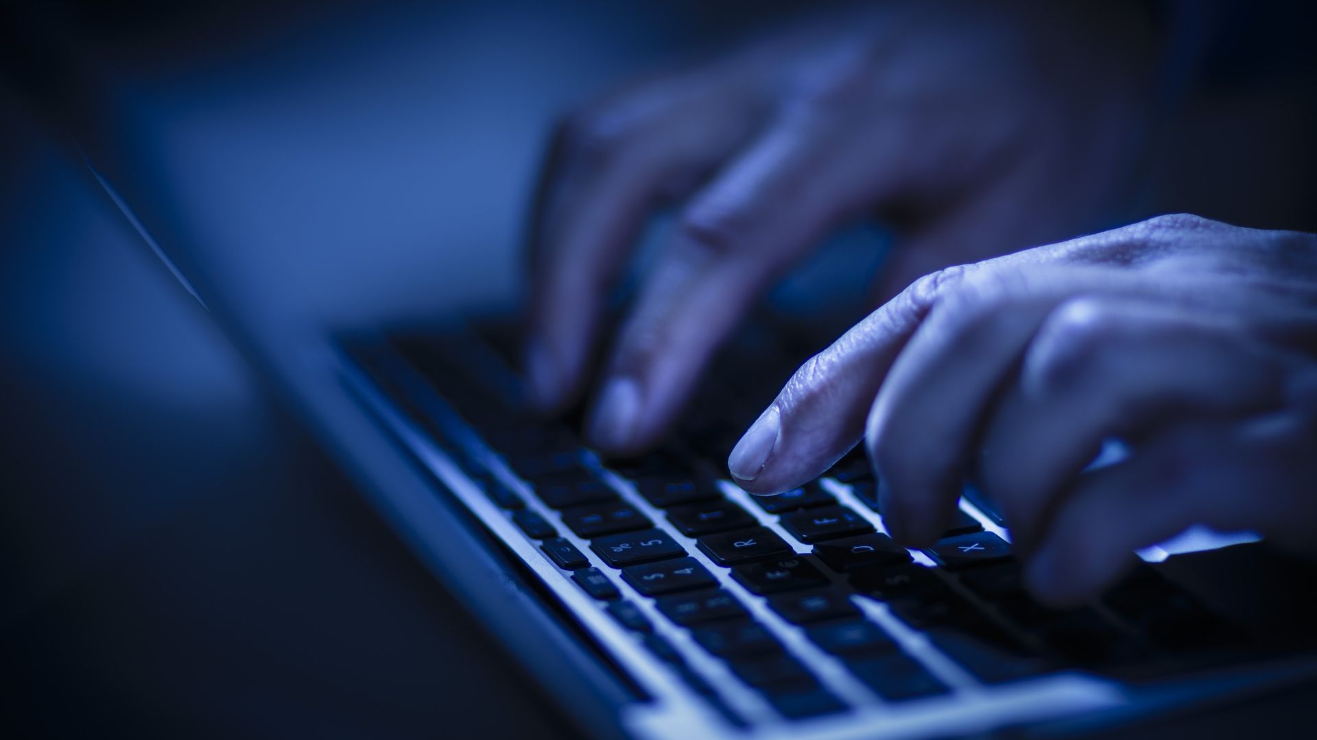 Fingers type on a laptop in blue light