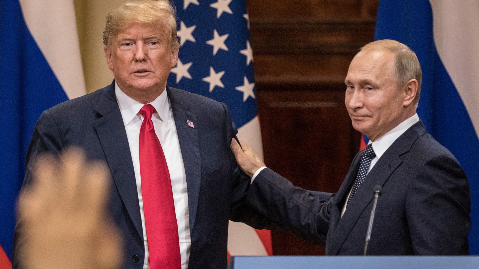 Vladimir Putin puts his hand on President Trump's arm as they look out at a crowd