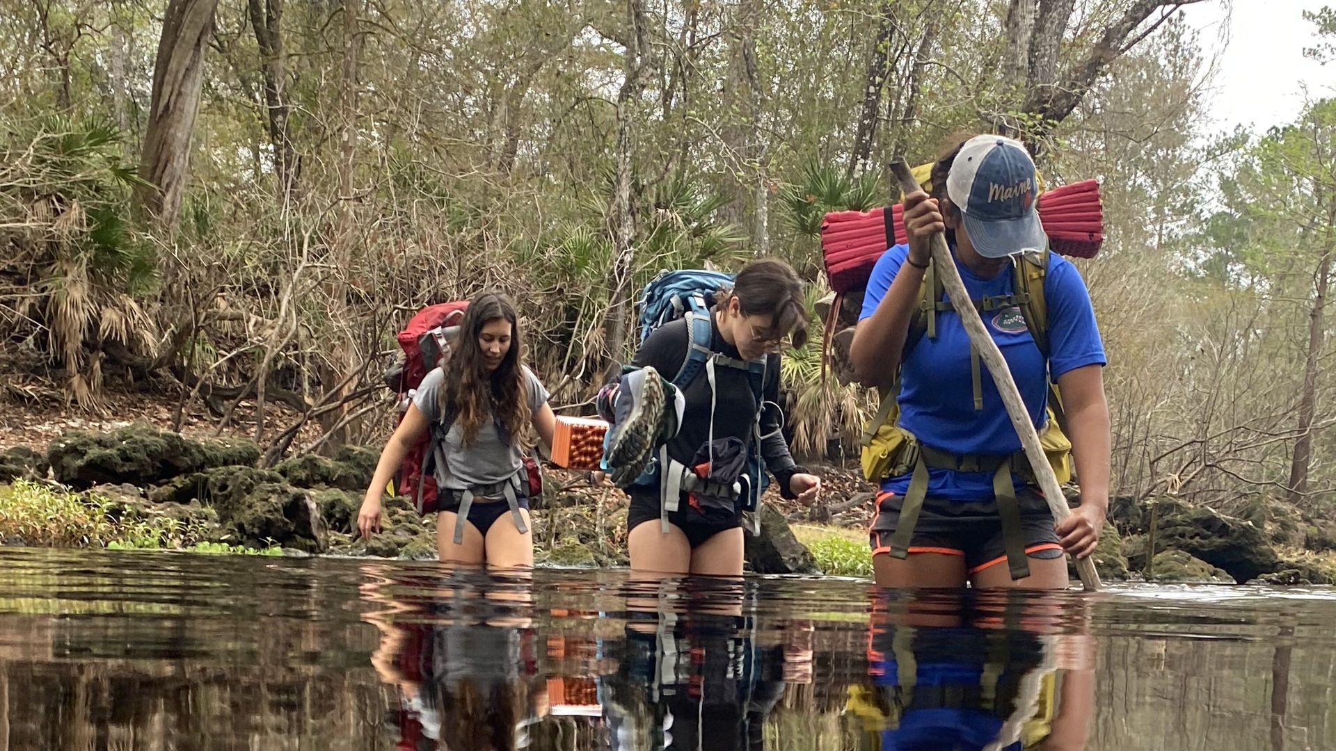 Three teenage girls hiking through a swamp