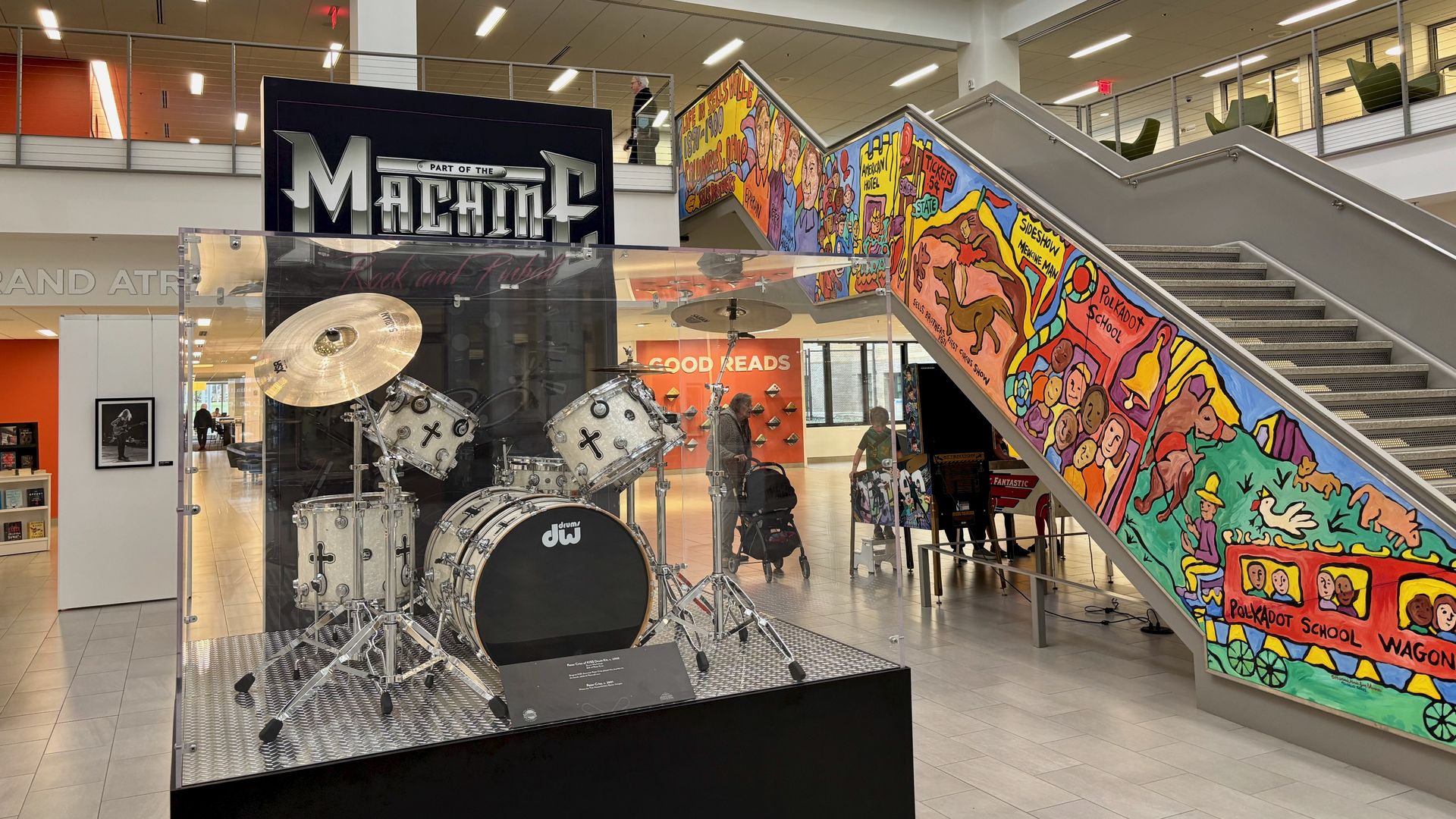  A Kiss drum set sits in the Main Library atrium near a staircase with a sign that reads "Part of the Machine: Pinball and Rock"