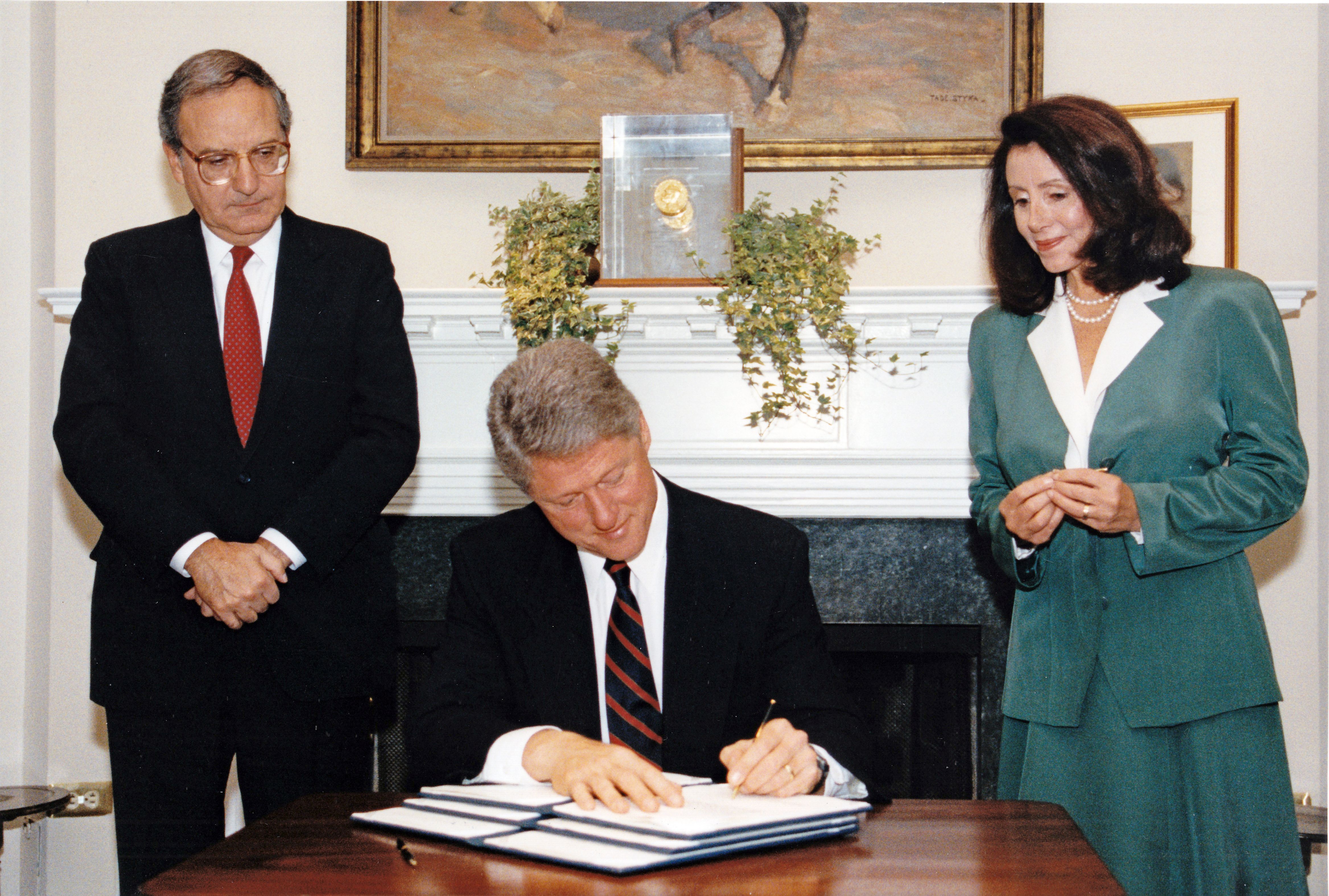 George Mitchell, Nancy Pelosi and President Clinton stand in the Roosevelt Room as Clinton signs an executive order.