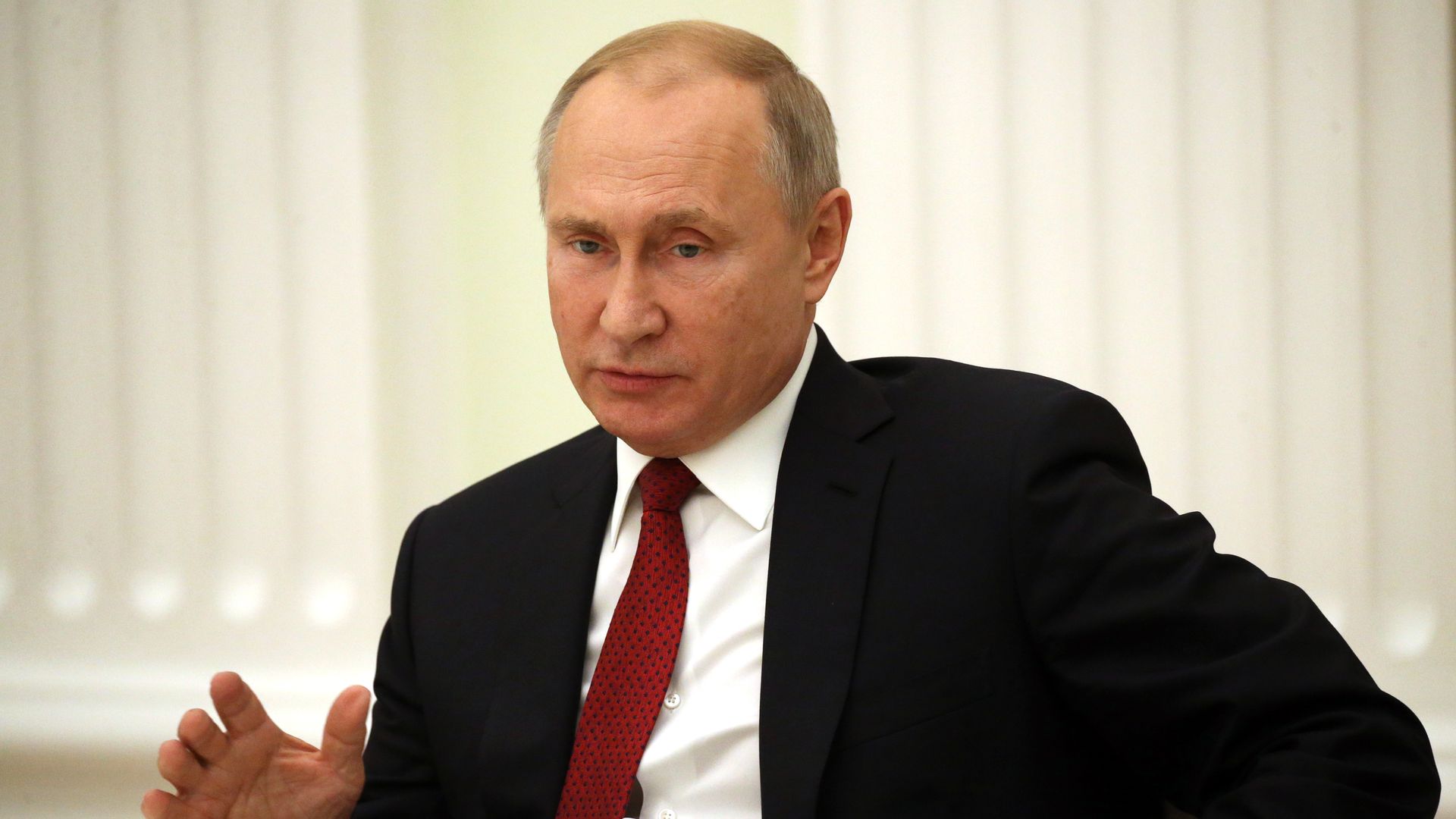 Vladimir Putin sitting in a chair in a suit and tie