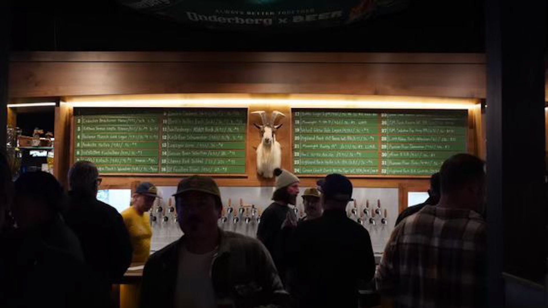 A dark bar with a green chalk board and a  stuffed ram's head trophy