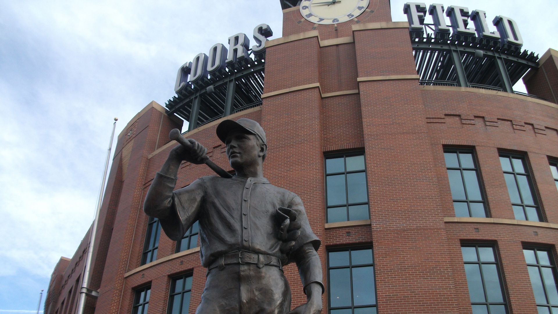 A photo of the outside of Coors Field in Denver. A statue of a baseball player is in the foreground