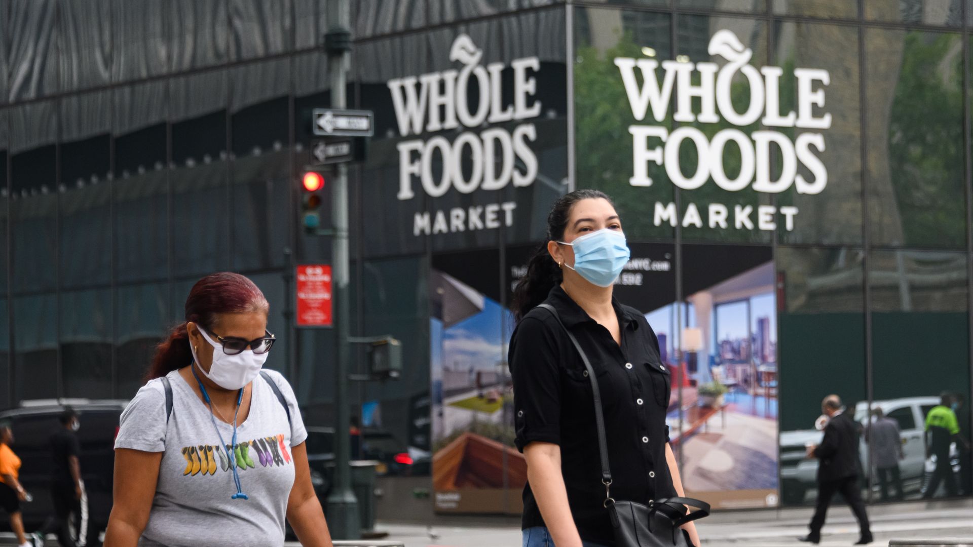 Whole Foods sign on store with two people in the foreground walking with masks on