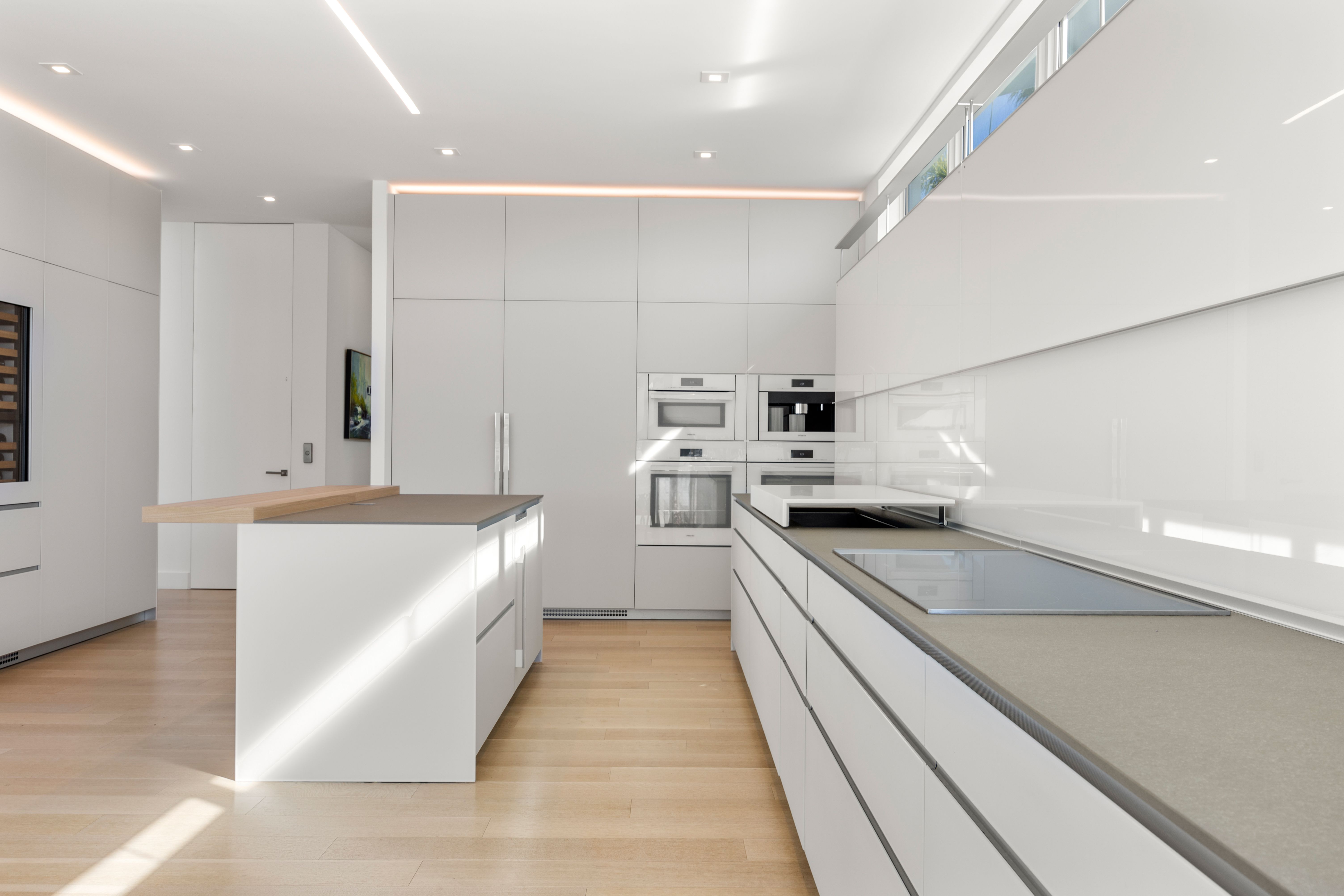 A sleek, white modern kitchen with light wood floors.