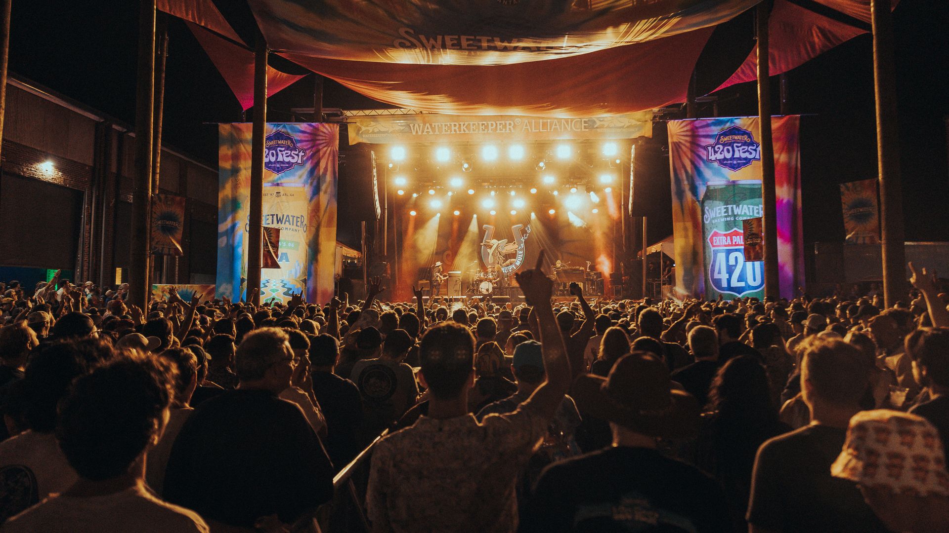 A photo of a crowd watching a brightly lit stage where a band is performing under a banner that says "Waterkeeper Alliance"