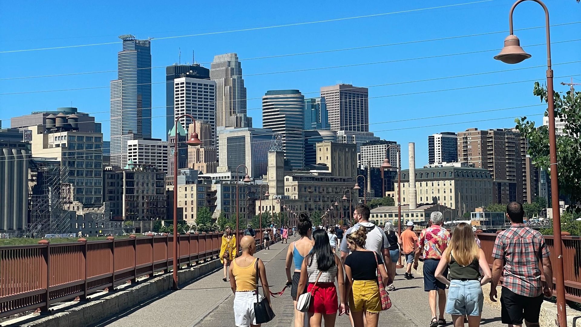 People walk on the stone arch bridge witht he minneapolis skyline in the distance