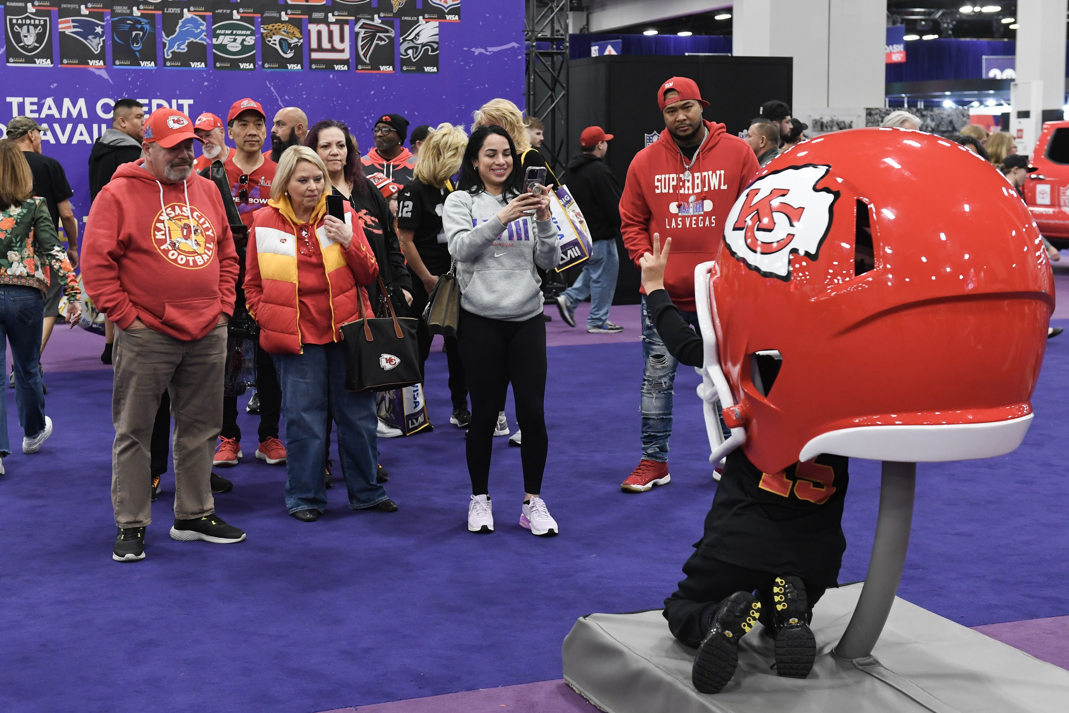 A family crowds around an oversized Kansas City Chiefs helmet while a person stands inside and poses for a photo.