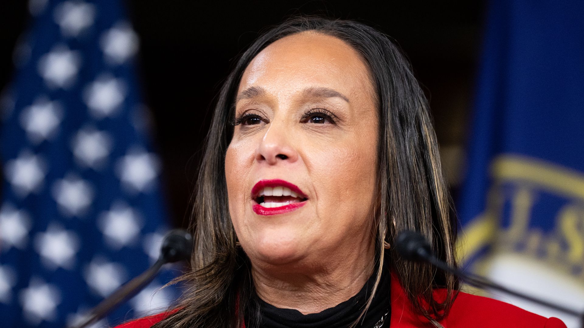 Monica de la Cruz speaks in front of a set of flags.