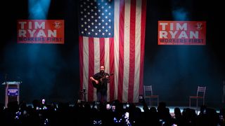 Dave Matthews Band se produisant sur scène devant un drapeau américain et un panneau de campagne de Tim Ryan. 