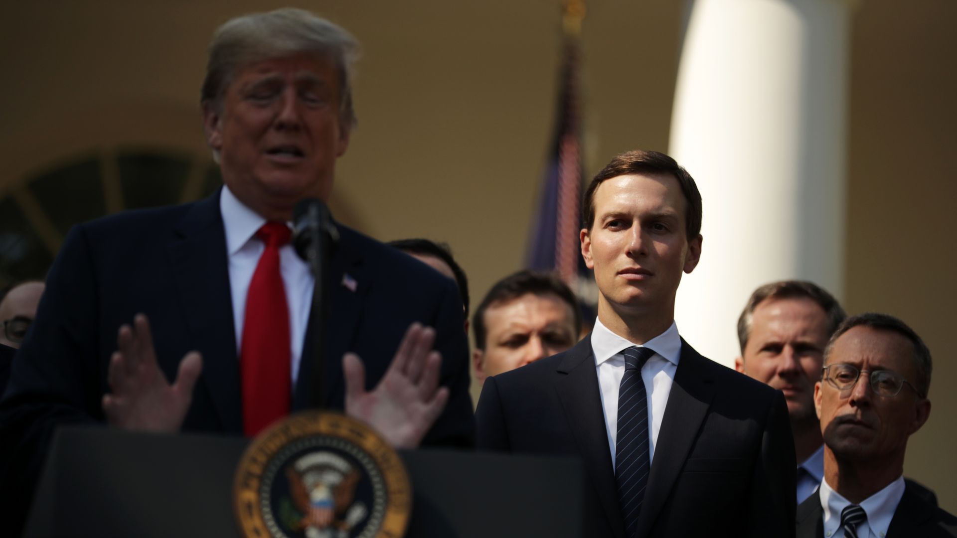 Jared Kushner standing behind President Trump while he gives a speech. 