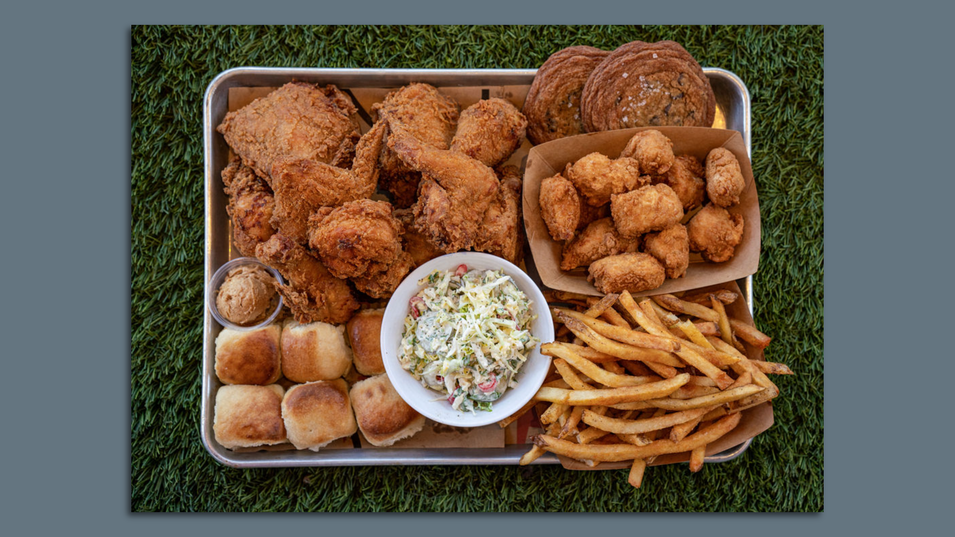 A tray filled with fried chicken, French fries, bread rolls, cole slaw and cookies. 