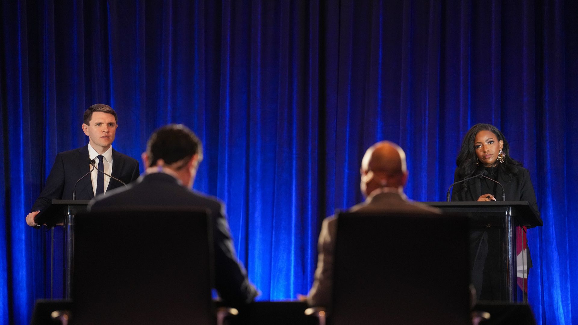 State Rep. James Talarico, left, and U.S. Rep. Jasmine Crockett stand at podiums with microphones in front of a blue curtain, facing two seated people.