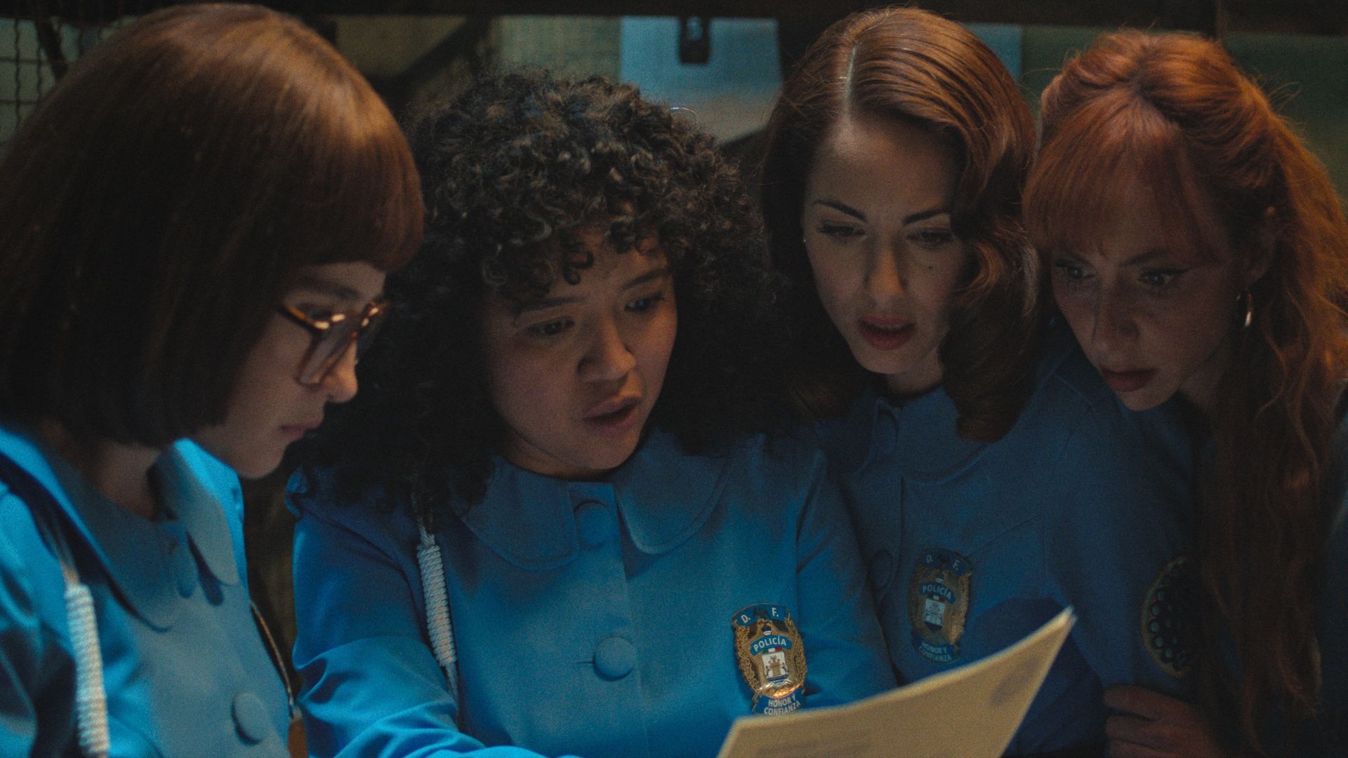 Four women in blue look down at a piece of paper