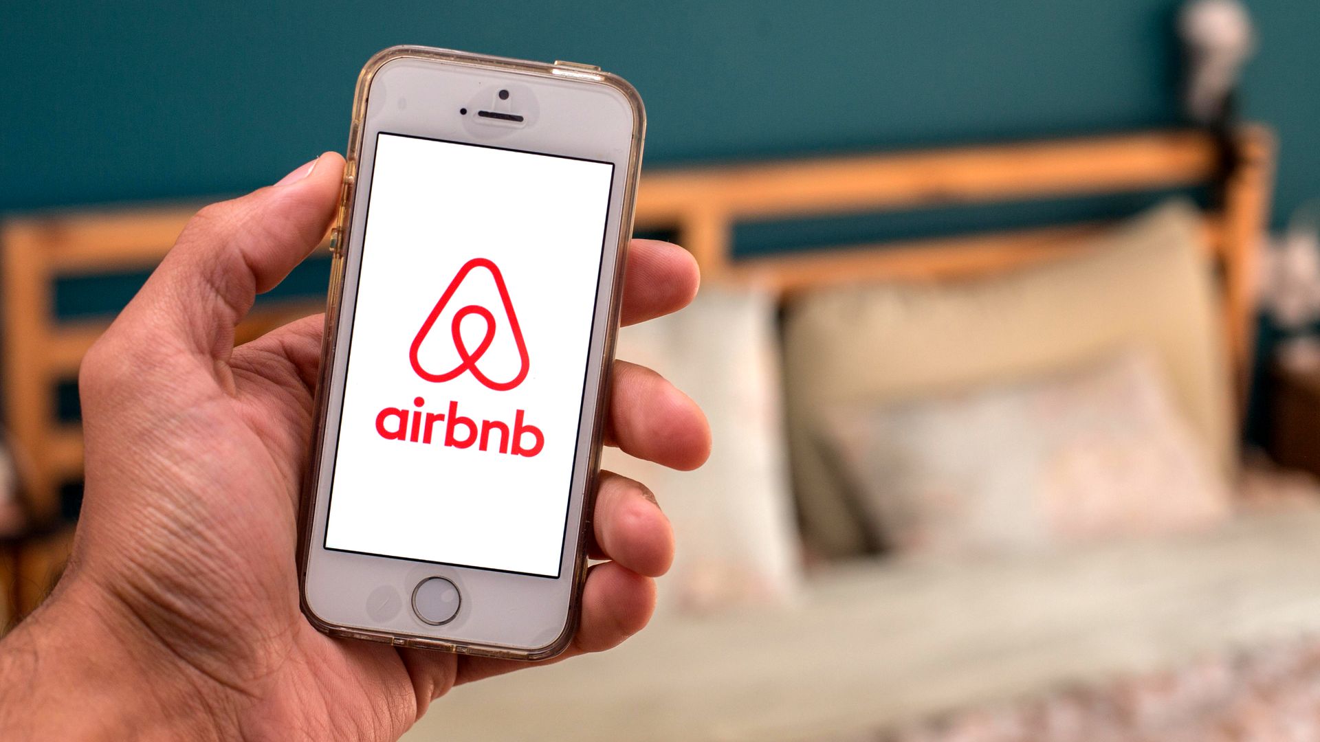 A photo illustration of the Airbnb logo with a bed in the background