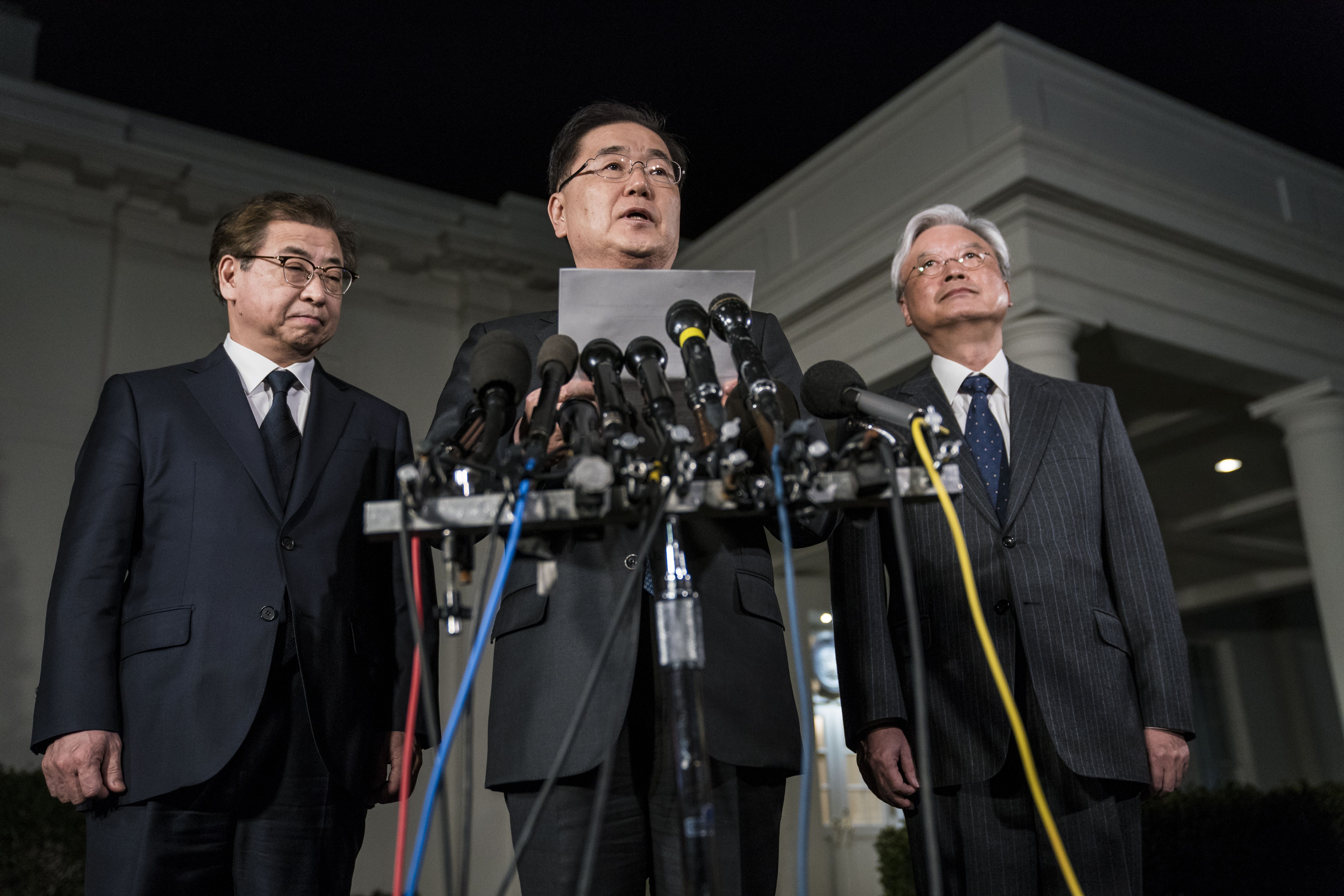 Three South Korean officials stand around microphones in the dark outside the White House.