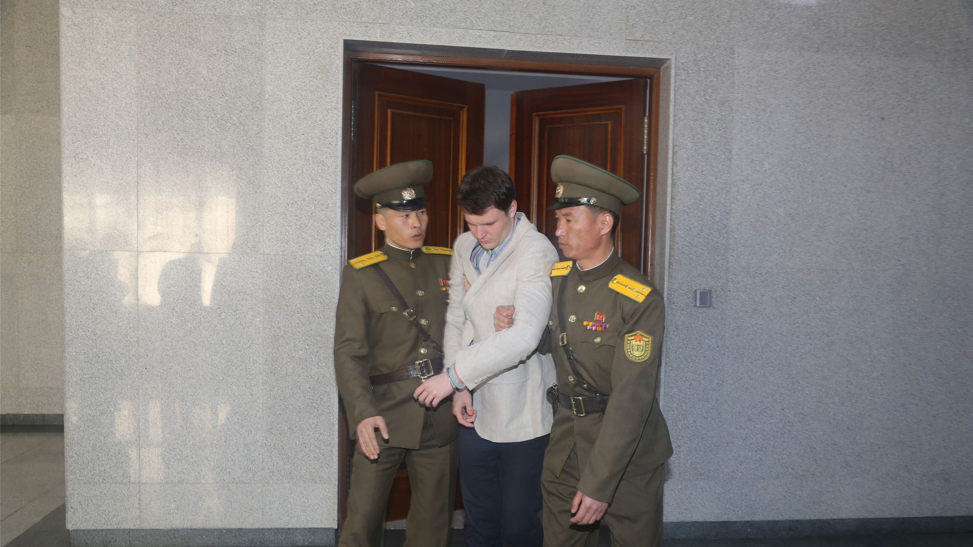 In this image, Otto Wambier is led through a doorway by two North Korean guards.