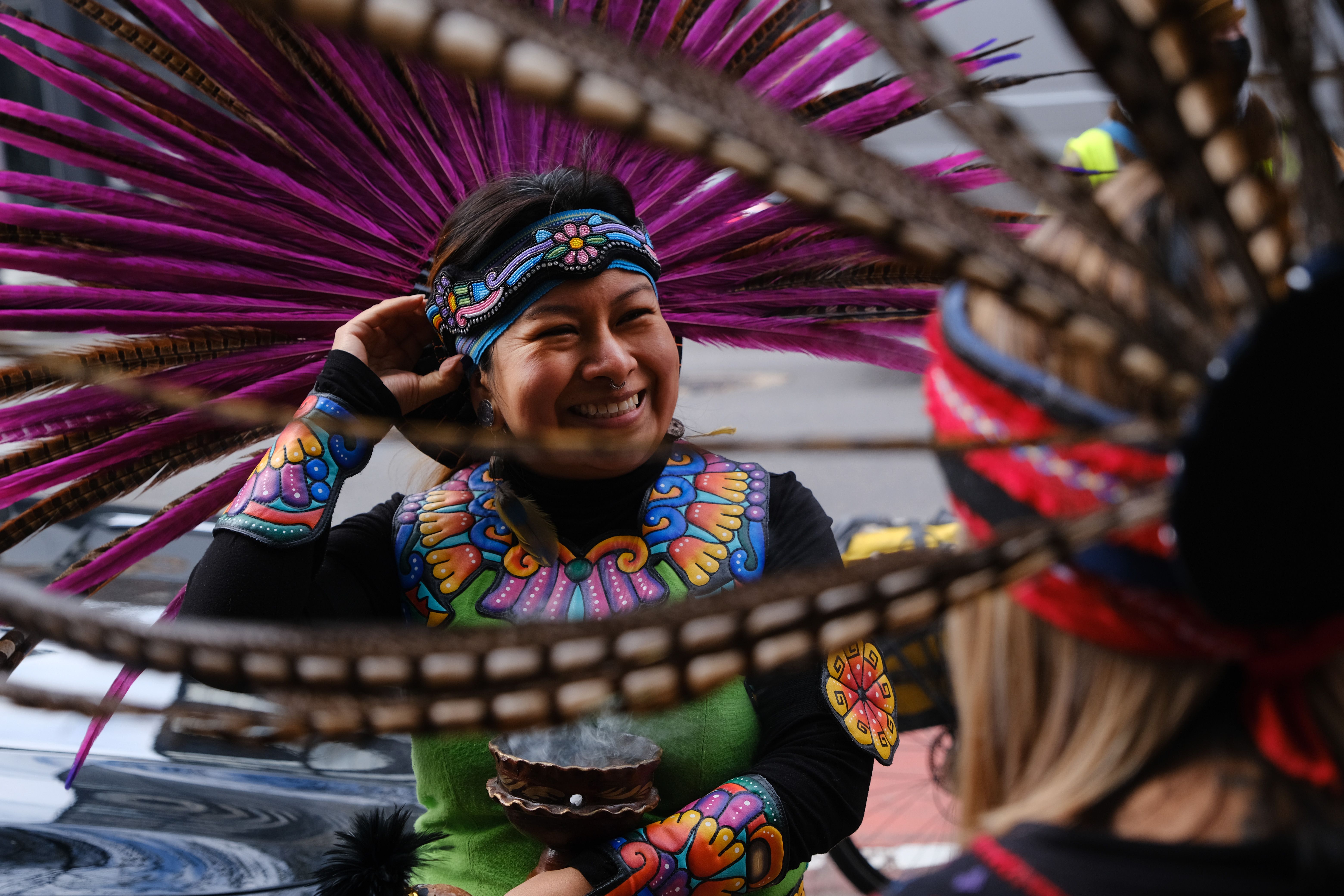 A person smiles while wearing a feathered headdress.