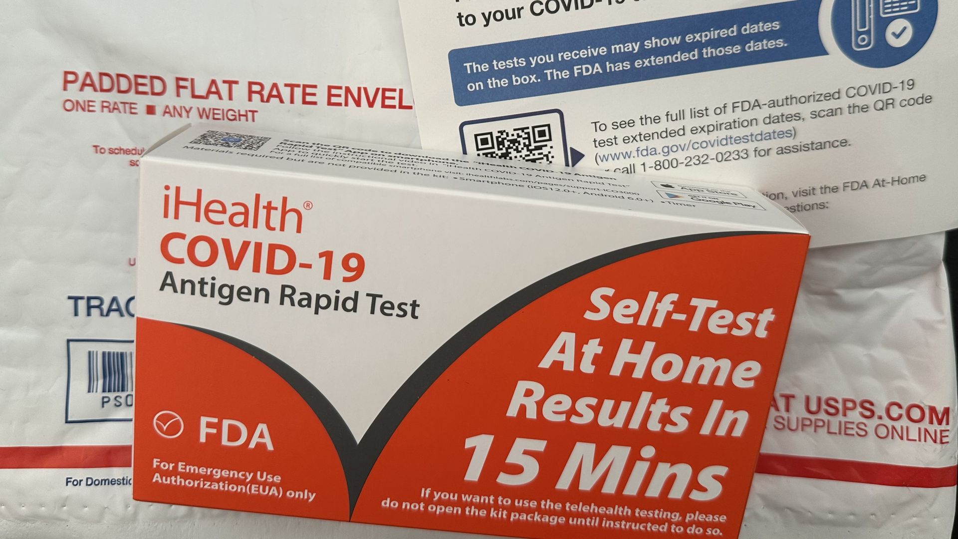 COVID test kit on top of USPS padded envelope with a postcard explaining test expiration dates
