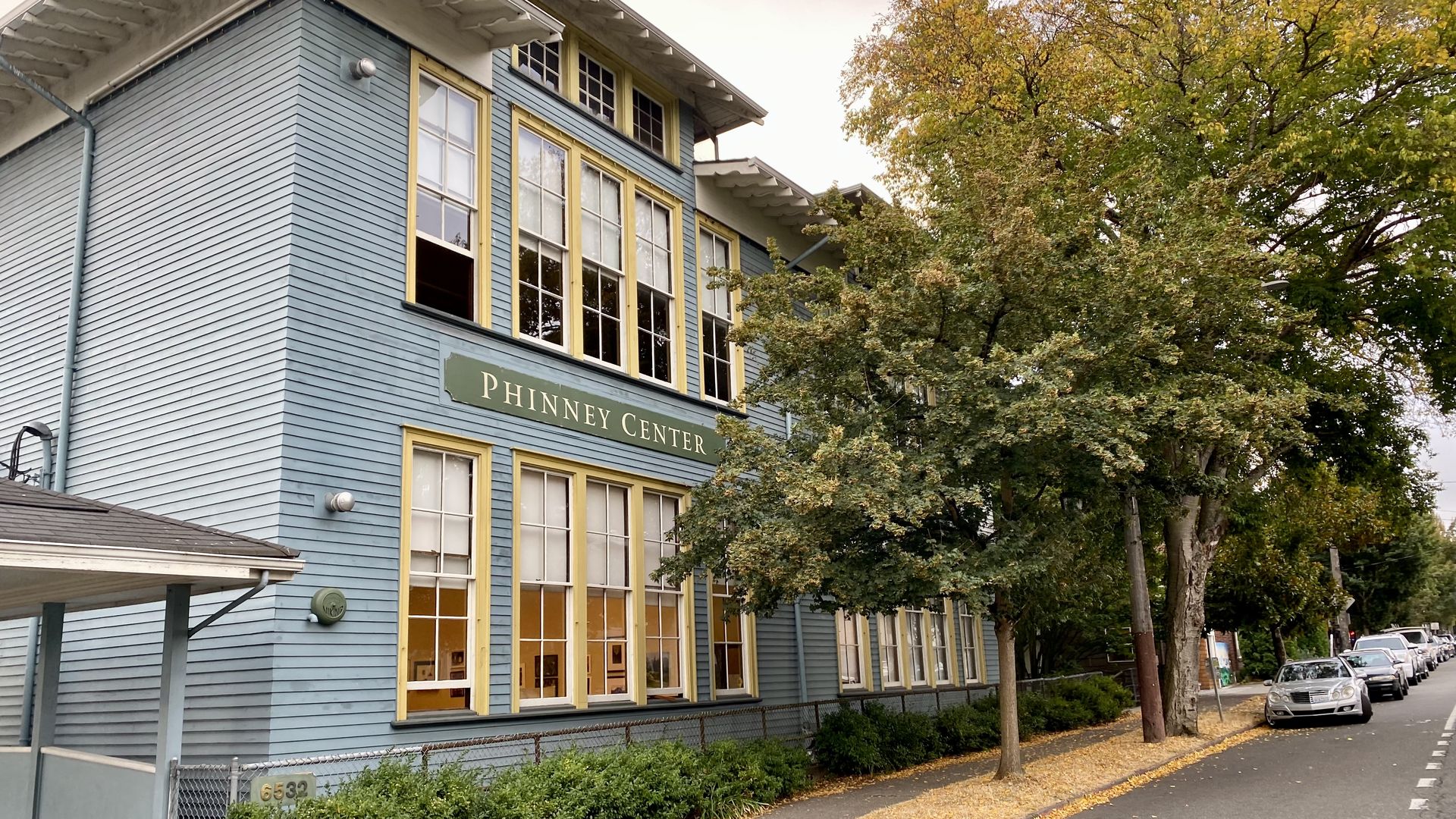 A blue building that says "Phinney Center" on it with a tree next to the sidewalk.