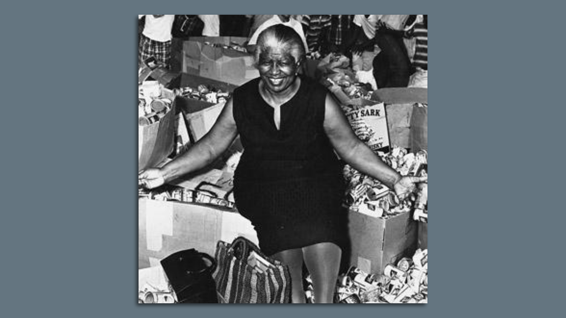 A black and white image of a woman sitting in front of boxes and cans