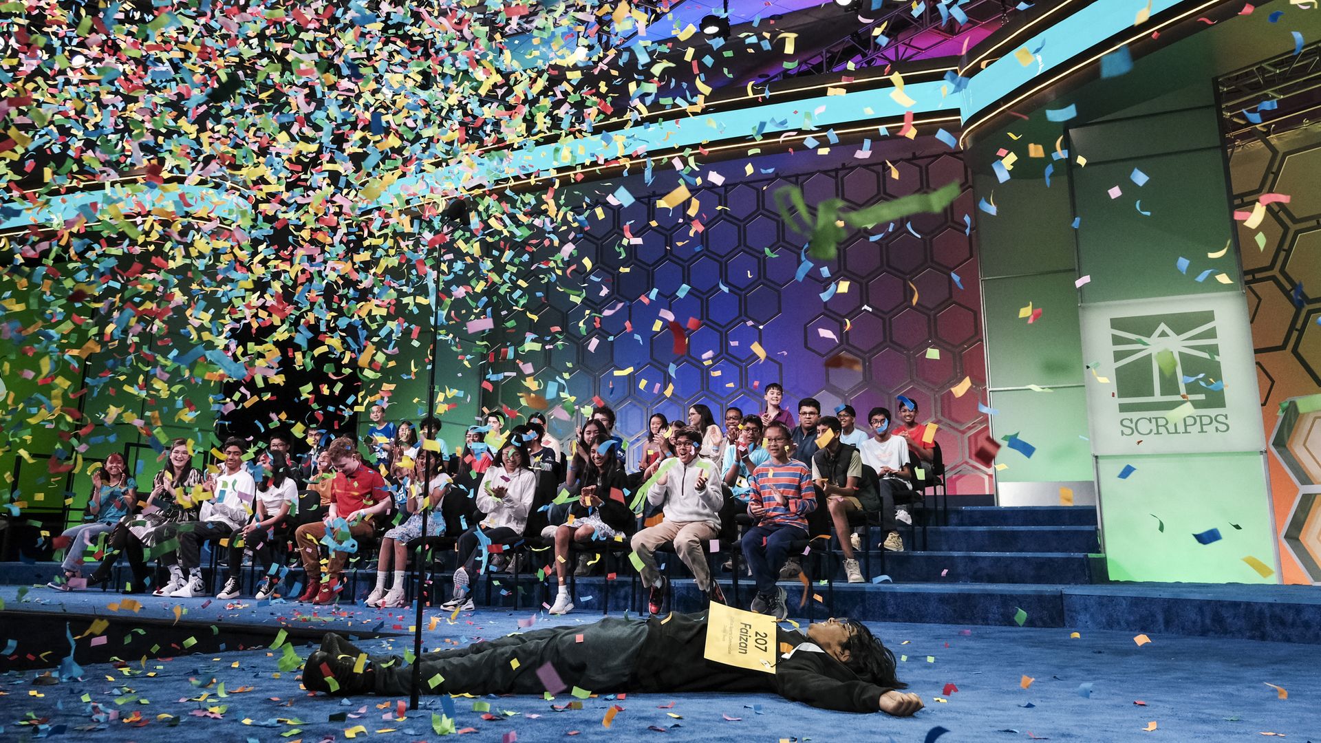 Image shows a boy laying on the ground with confetti falling on him.