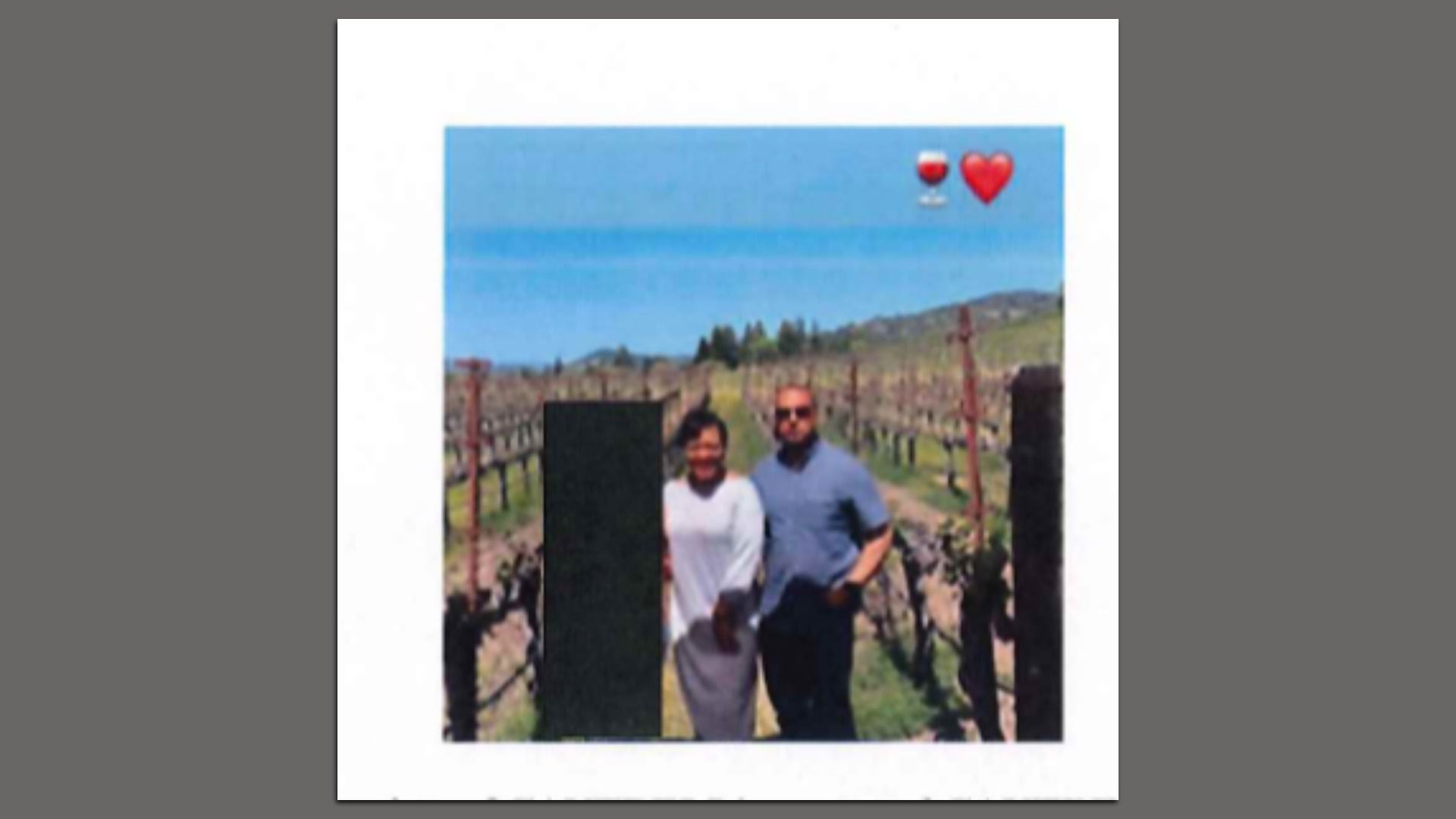 A couple stands in a vineyard under a blue sky. The woman wears a white outfit, and the man wears a blue shirt and sunglasses. Wine glass and heart emojis appear above.