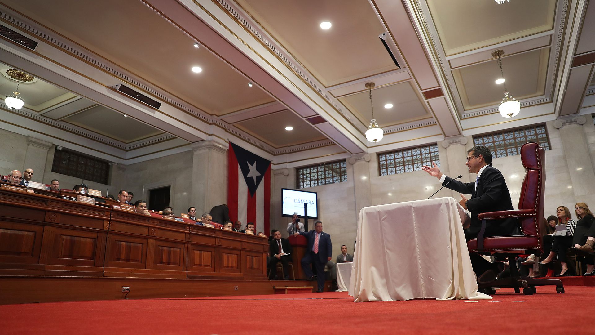 In this image, Pedro sits in the Puerto Rican House of Representatives and speaks to a panel