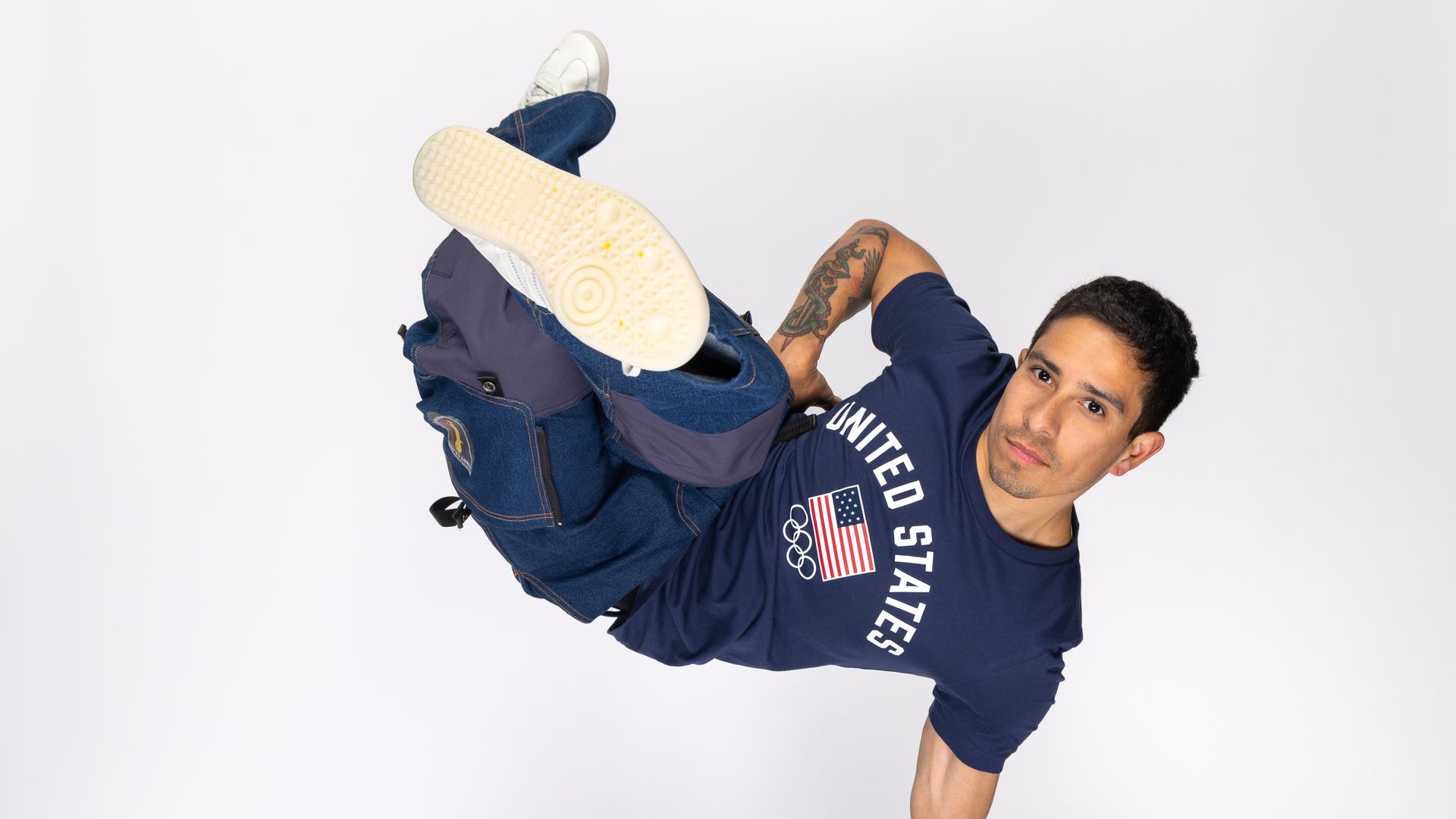Victor Montalvo, a breaking champion, lifts his whole body up with one arm while wearing United States Olympics team t-shirt. 