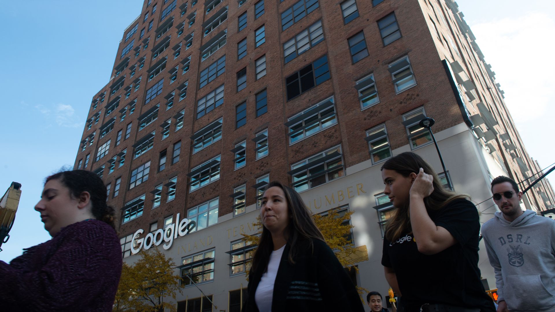 A group of people walk in front of a building with a white "Google" sign