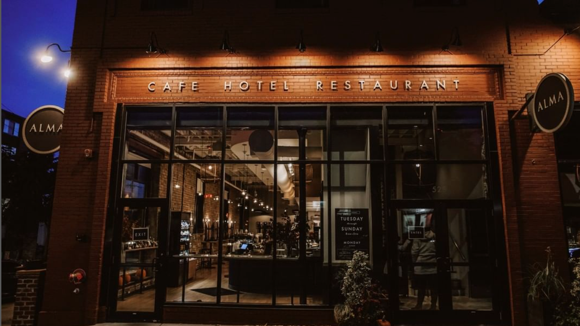 A restaurant front as seen at night with plenty of windows. People can be seen inside.