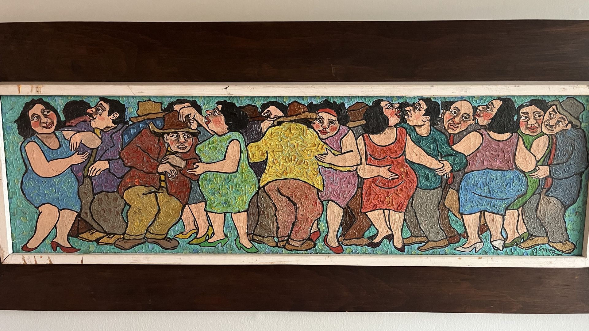 Colorful mural of a crowded dance scene: people in bright dresses and hats, dancing arm-in-arm along a teal background; bold, textured brushstrokes framed by a white wall and dark wood trim.