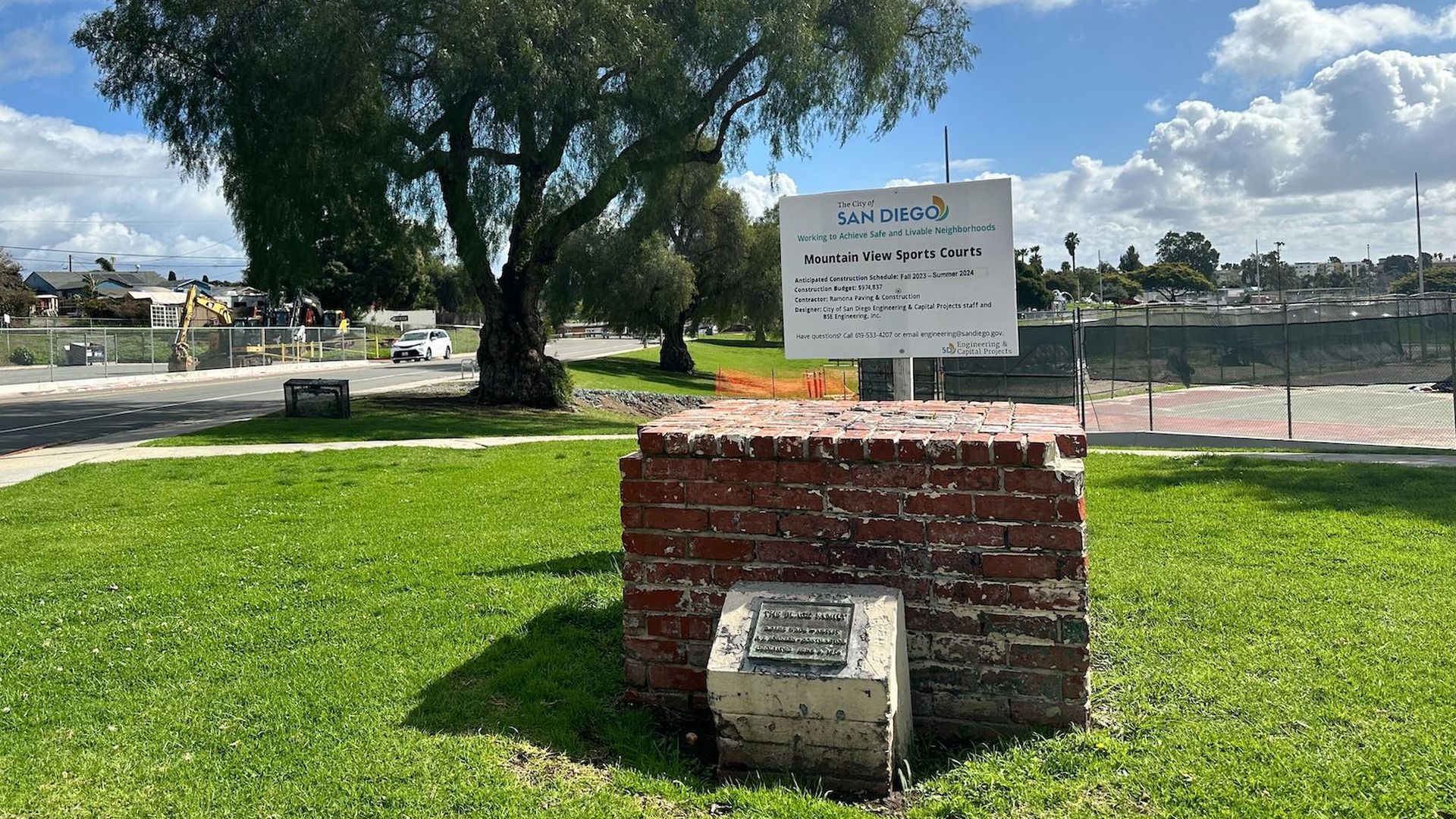A brick base with a plaque where a statue once stood at a grassy park.